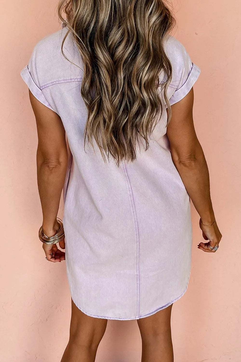 Back view of model in the button down short sleeve denim dress with pockets, featuring a clean design and relaxed fit. A versatile addition to any wardrobe.