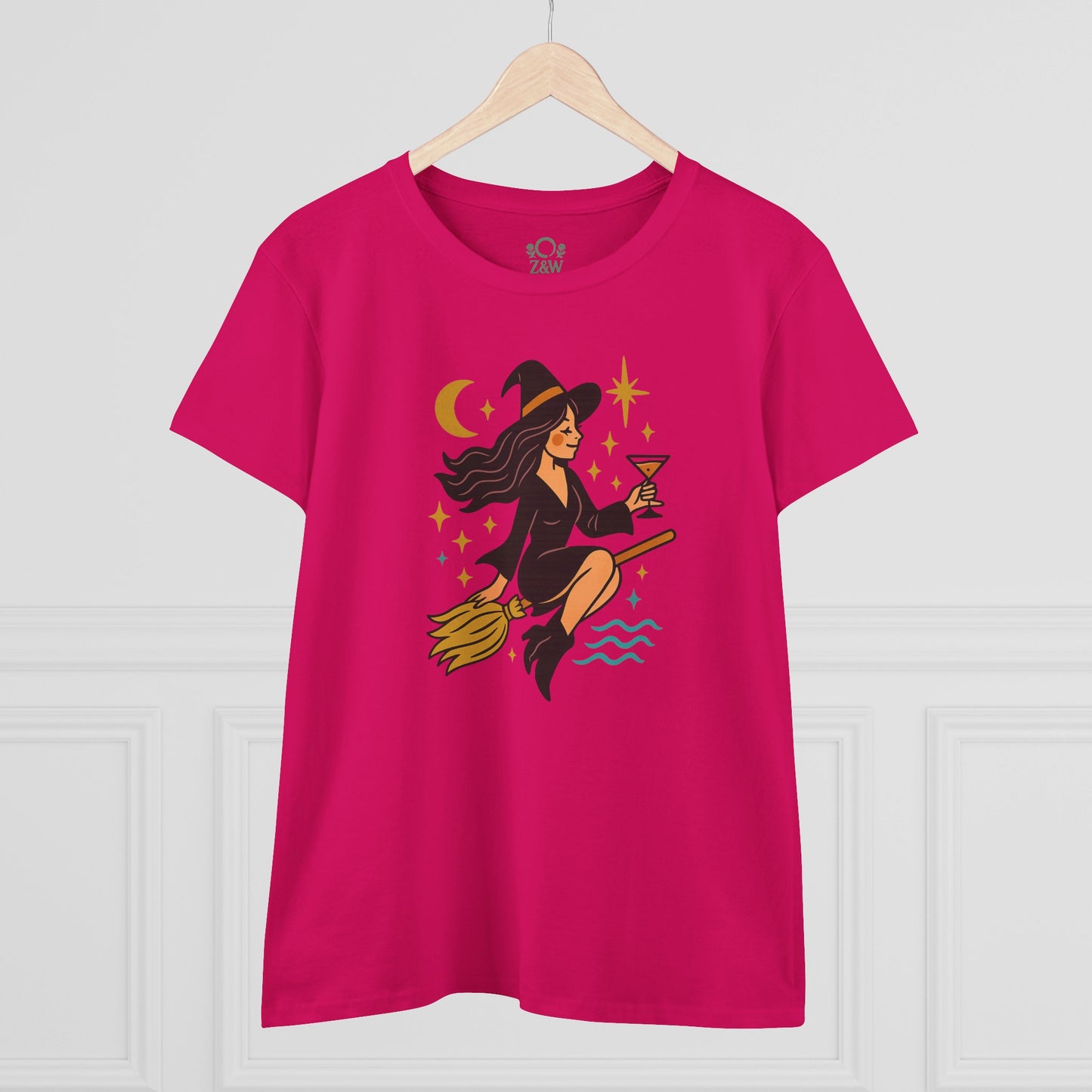 Witchy Night Out Tee featuring a stylish witch character holding a cocktail, designed for comfort and durability, displayed on a wooden hanger.