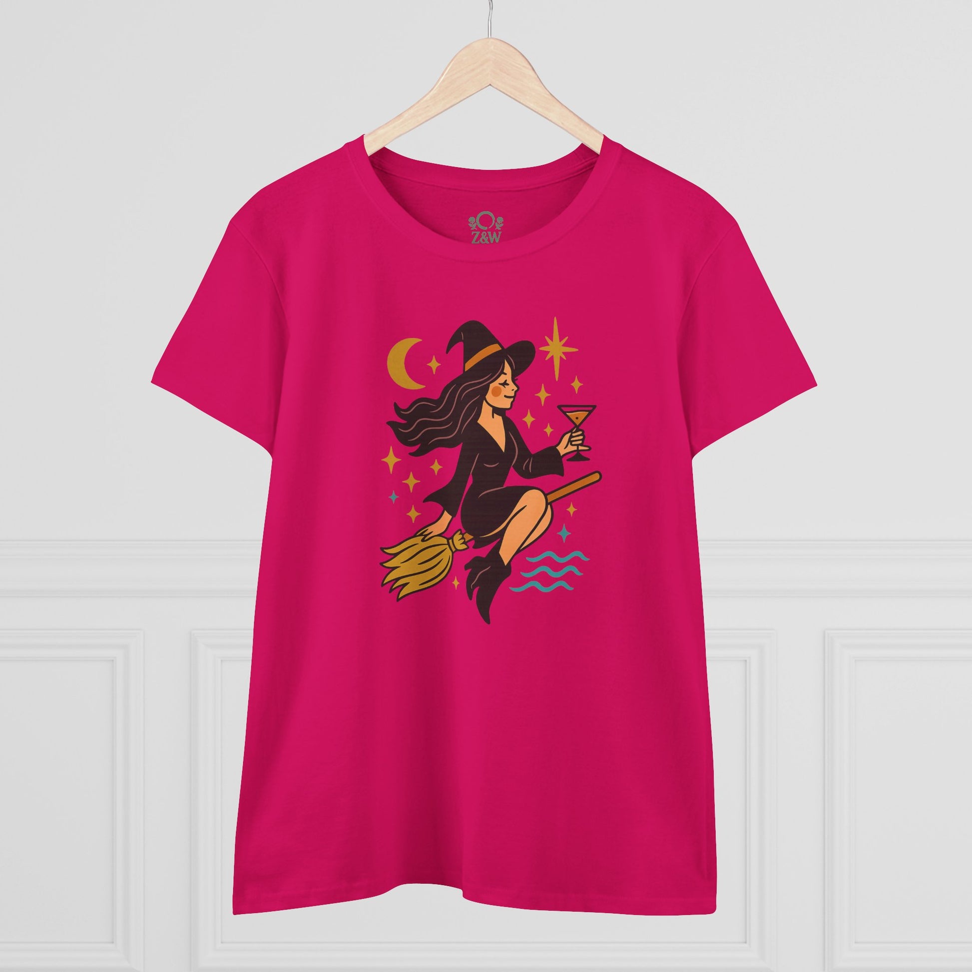 Witchy Night Out Tee featuring a stylish witch character holding a cocktail, designed for comfort and durability, displayed on a wooden hanger.