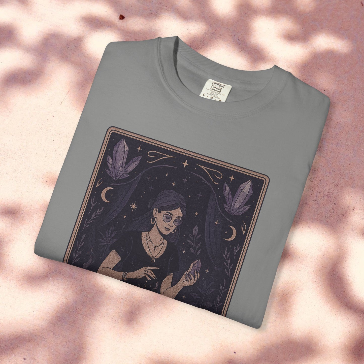 Intuitive Tarot Tee in a light gray color, placed on a soft pink backdrop, illustrating a woman engaged in tarot reading with crystals, crafted from premium 100% cotton.