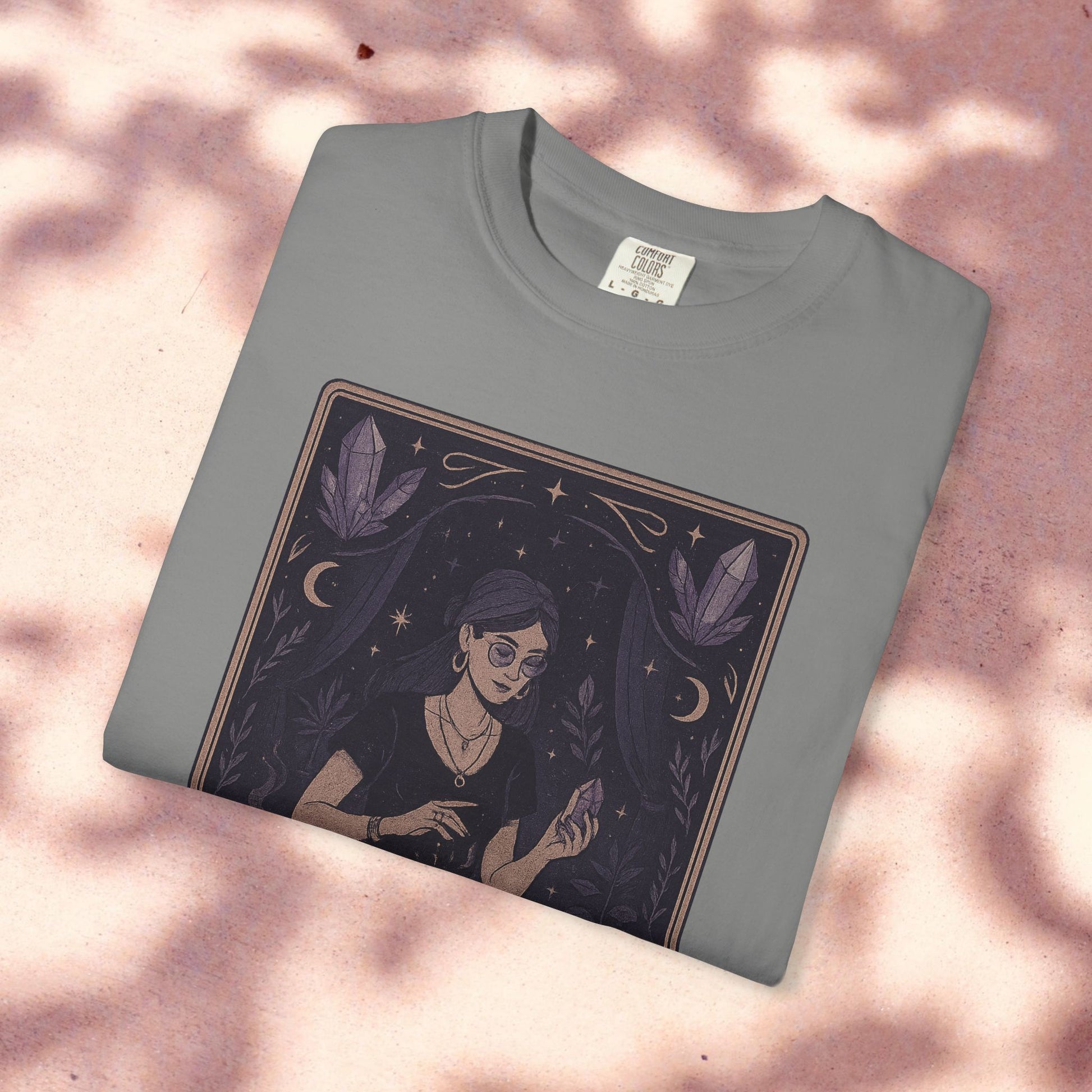 Intuitive Tarot Tee in a light gray color, placed on a soft pink backdrop, illustrating a woman engaged in tarot reading with crystals, crafted from premium 100% cotton.