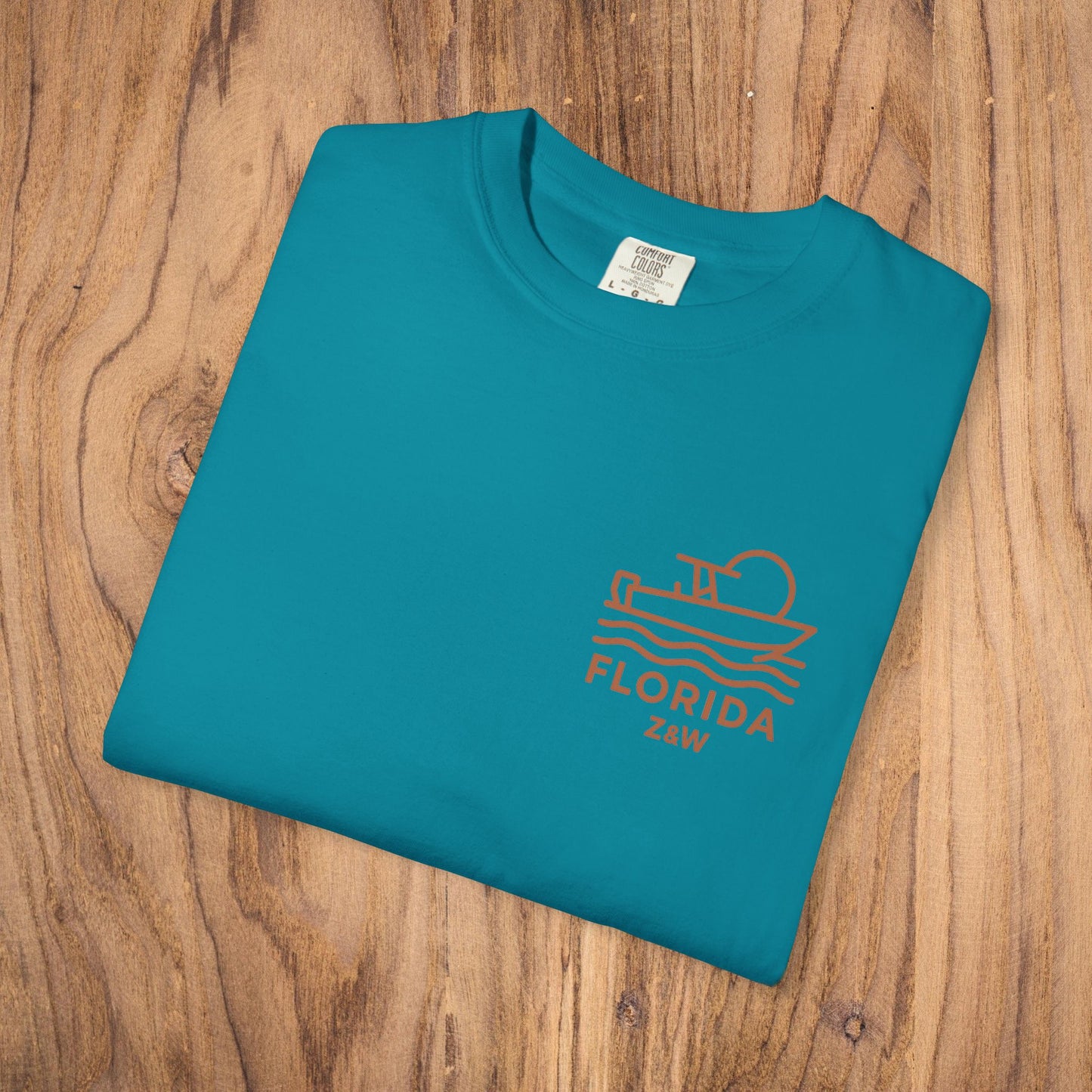 Unisex Florida Graphic Tee in vibrant teal color, garment-dyed for a relaxed fit, resting on a wooden table.