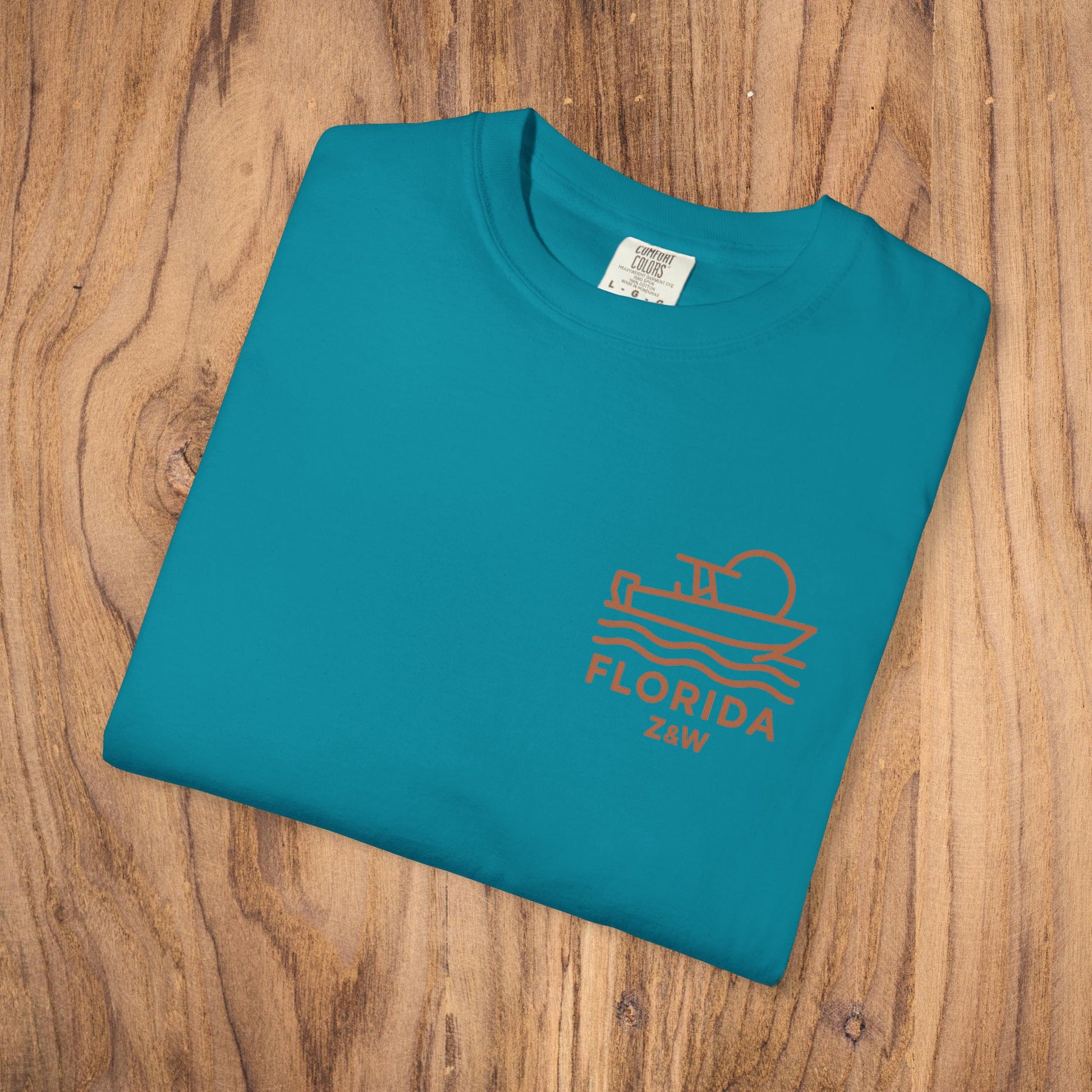 Unisex Florida Graphic Tee in vibrant teal color, garment-dyed for a relaxed fit, resting on a wooden table.