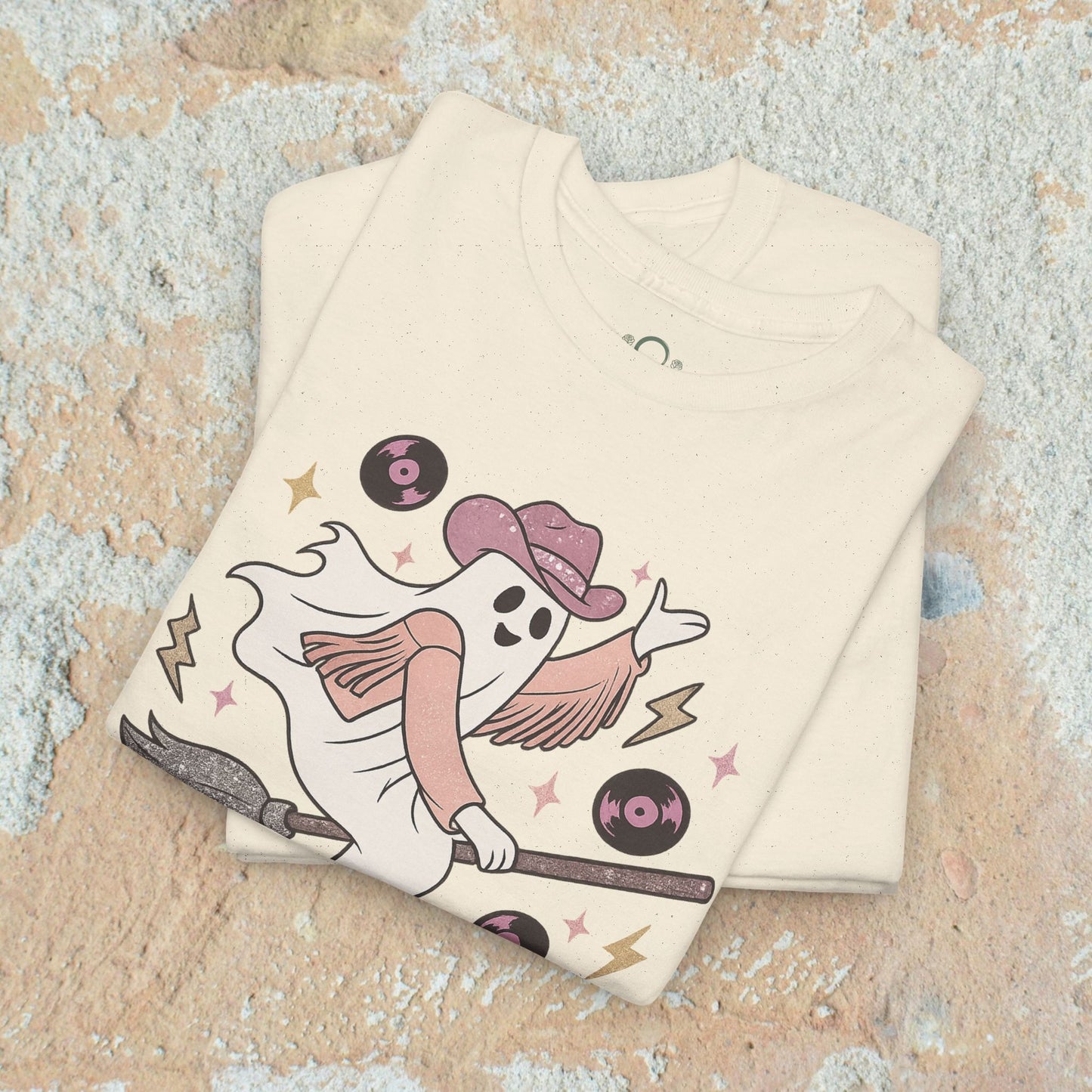 Spooky Cowgirl Graphic Tee - Soft Fabric, Eco-Friendly, Sizes S-5XL, displaying a whimsical ghost cowgirl on a broom, in a cream color tee with a vintage feel.