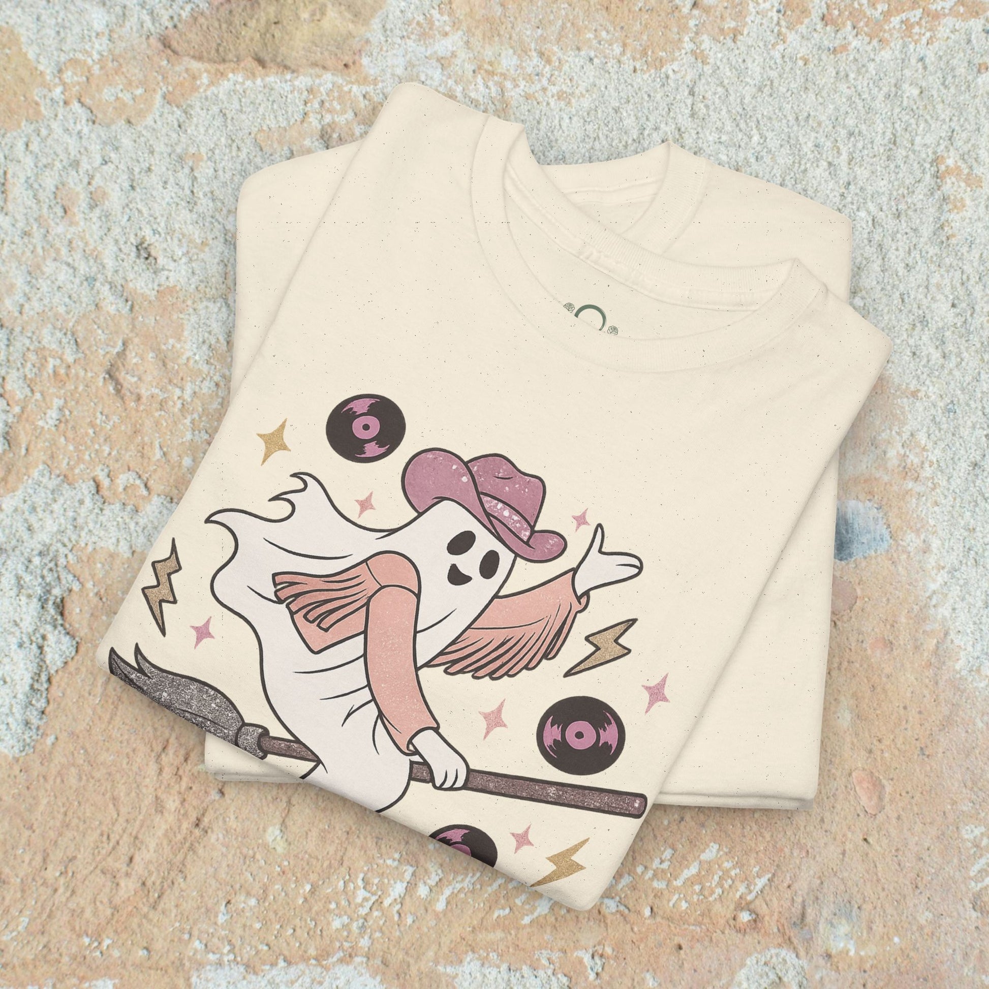 Spooky Cowgirl Graphic Tee - Soft Fabric, Eco-Friendly, Sizes S-5XL, displaying a whimsical ghost cowgirl on a broom, in a cream color tee with a vintage feel.