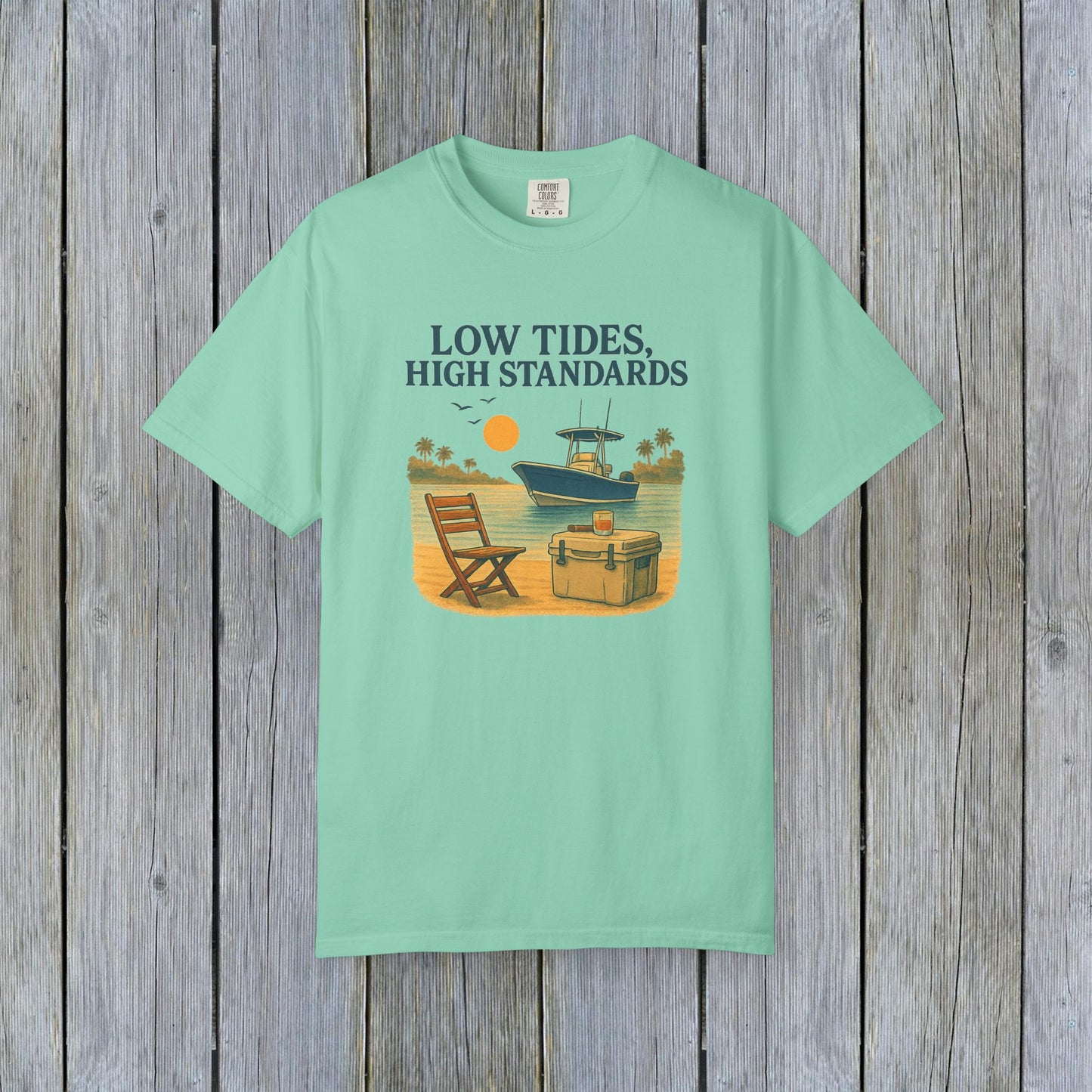 Garment-Dyed Low Tides High Standards T-Shirt in mint green. Features a beachy illustration depicting a chair and cooler next to a boat. Made from soft 100% US cotton, available in sizes S-4XL.