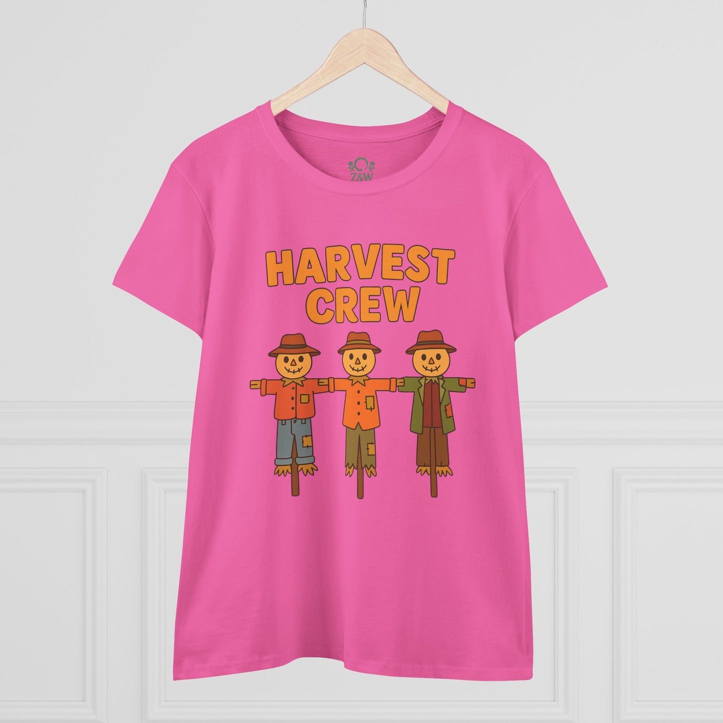 Front view of the Harvest Crew Halloween T-Shirt displayed on a wooden hanger, highlighting its vibrant pink color and playful scarecrow design.