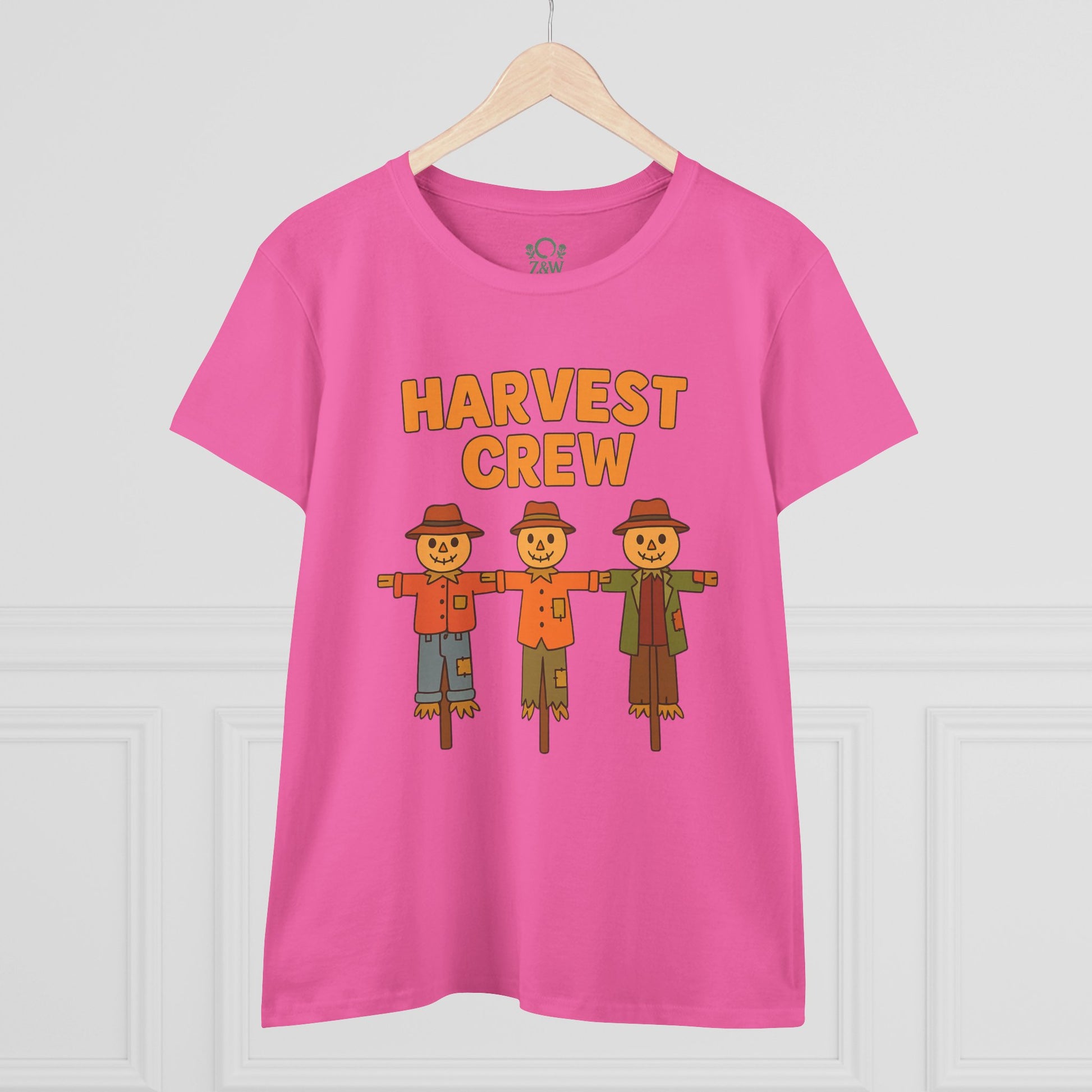 Front view of the Harvest Crew Halloween T-Shirt displayed on a wooden hanger, highlighting its vibrant pink color and playful scarecrow design.