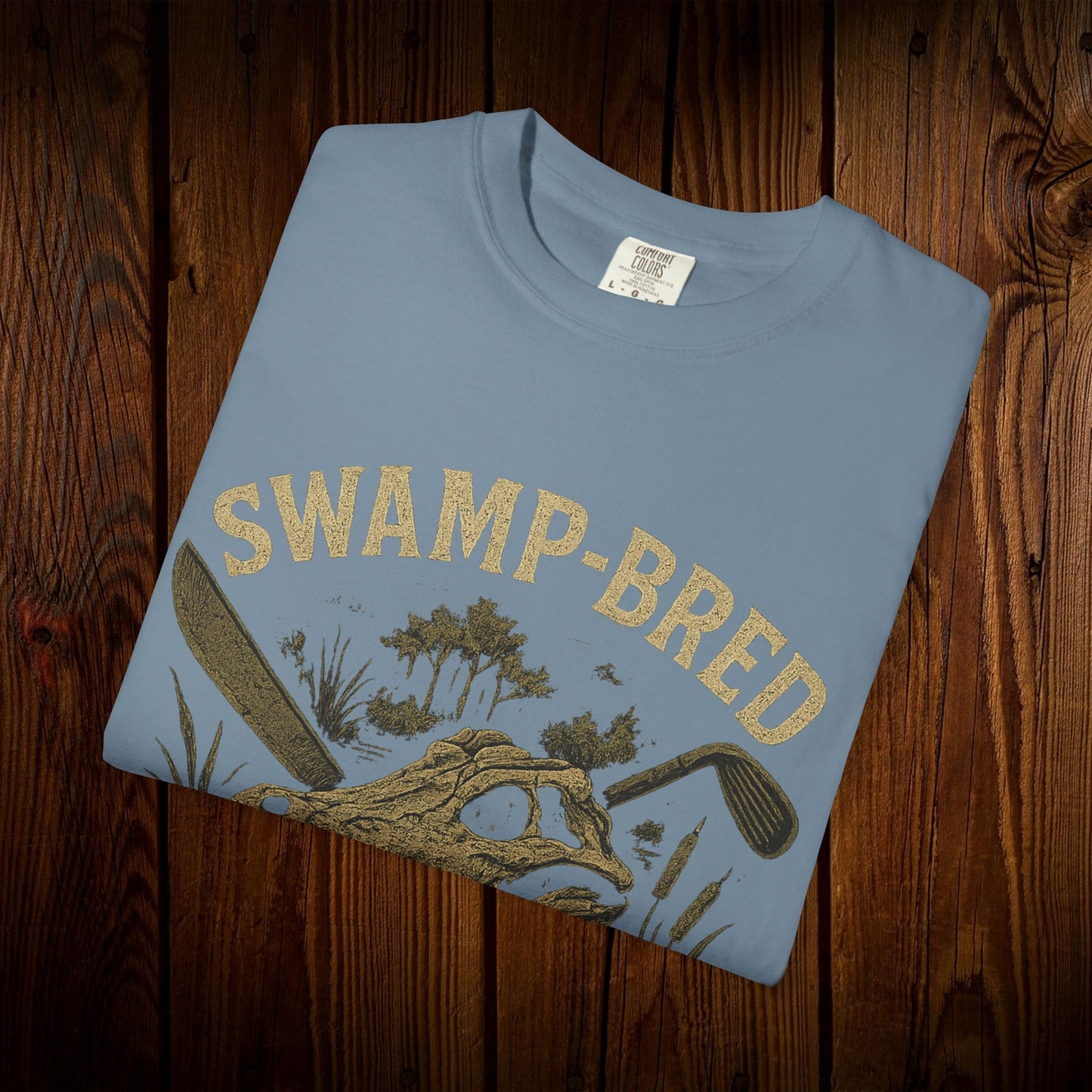 Unisex Swamp-Bred Fairway-Fed Tee in light blue, featuring a striking graphic design with swamp and golf elements, made from soft, durable pre-shrunk US cotton.