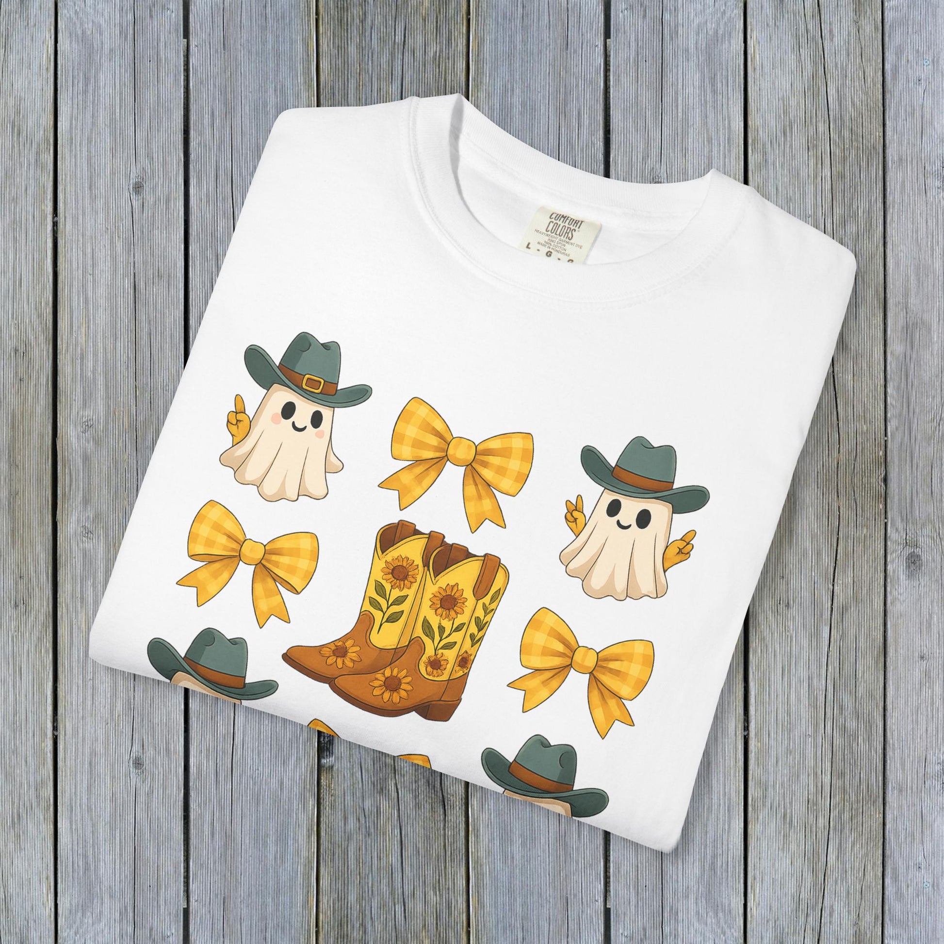 Cute Halloween T-Shirt design displaying playful ghosts, yellow bows, and cowboy boots, presented neatly folded against a rustic wooden backdrop, ideal for eco-conscious fall fashion.