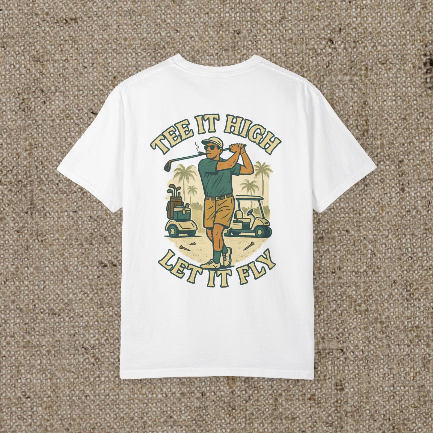 White Tee It High Let It Fly Graphic Tee displayed on a textured background, showcasing a colorful back graphic of a golfer with palm trees and golf carts.