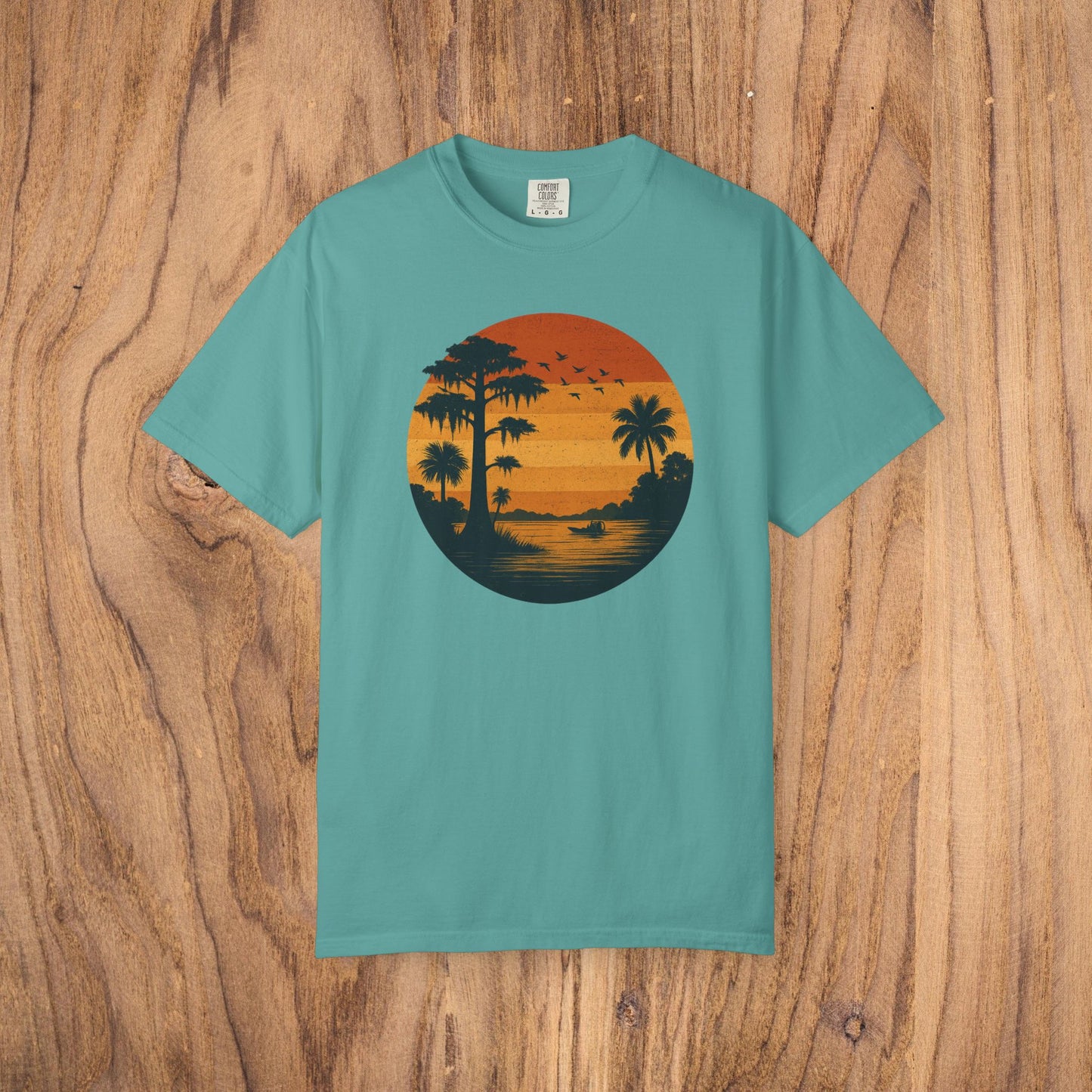 Unisex Garment-Dyed Sunset Tee in teal featuring a sunset motif with palm trees, designed for comfort and style, available in sizes S to 4XL.
