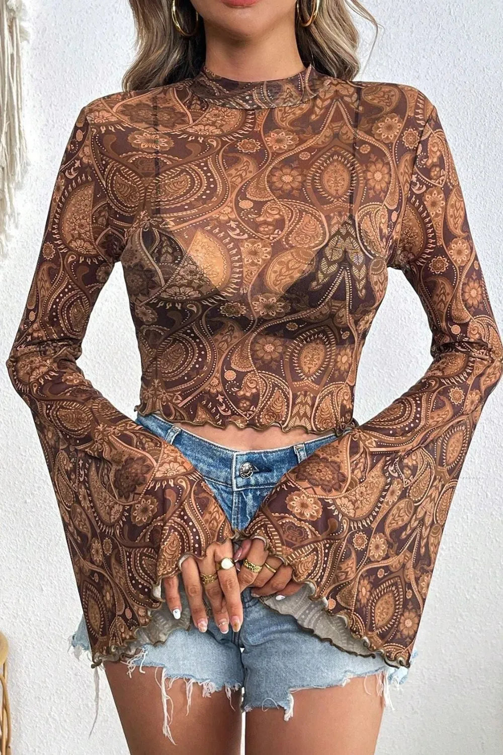 Stylish sheer printed mock neck top with flair sleeves, featuring a bohemian paisley pattern along with distressed denim shorts, perfect for a casual outfit.