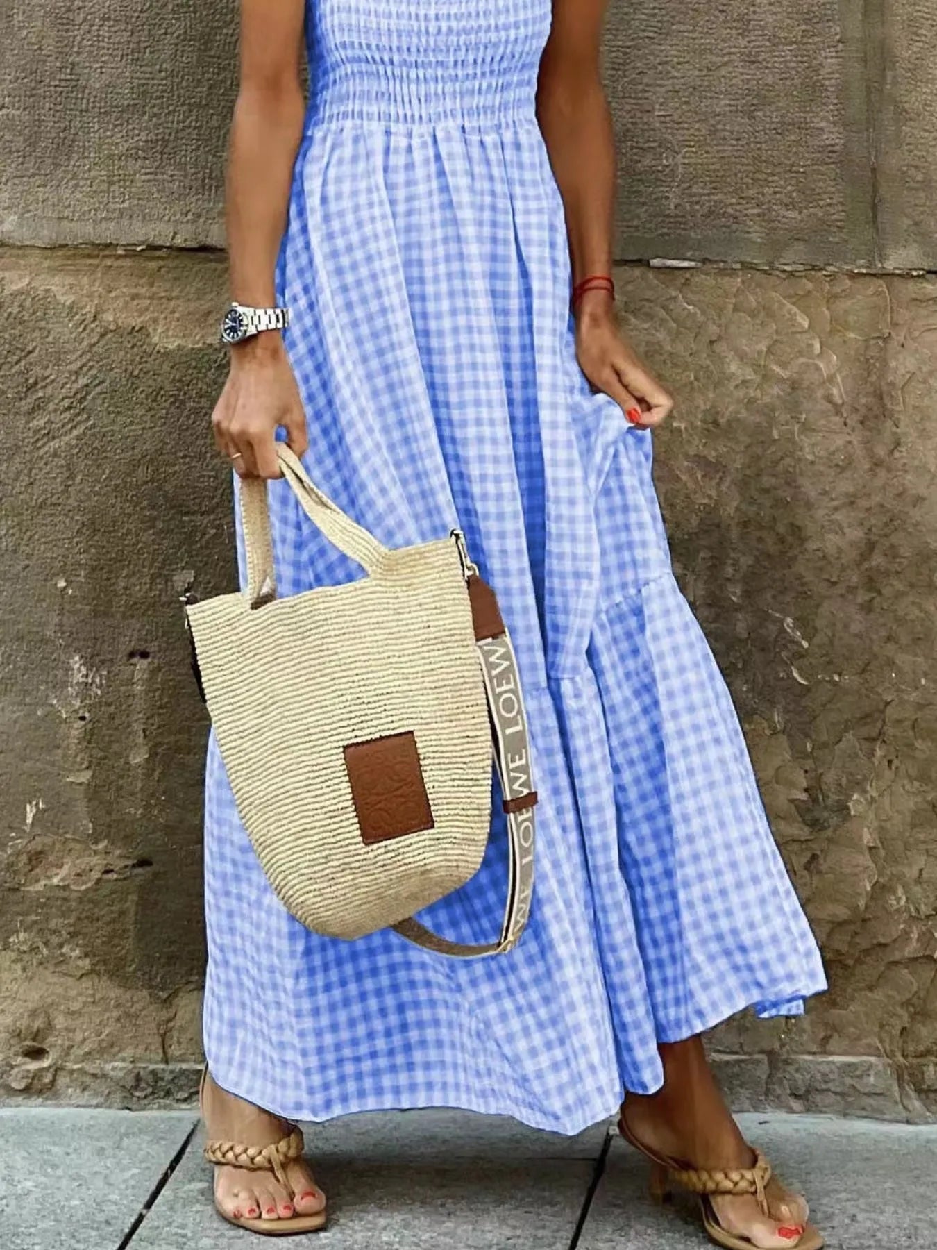 Close-up of a Gingham Maxi Dress with Ruffle Straps, Smocked Bodice & Tiered Design in blue and white, showcasing the dress's fabric detail and accompanying straw bag.