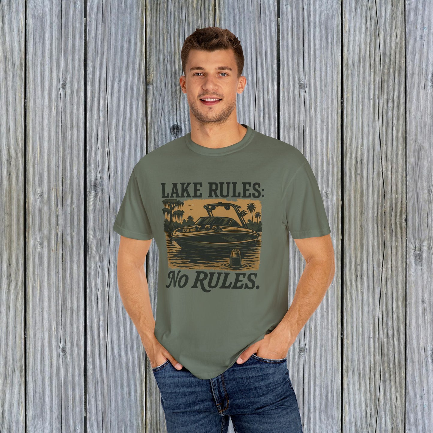 Unisex Garment-Dyed Lake Rules Tee displayed by a young man on a wooden background, featuring a boat graphic and the words 'Lake Rules: No Rules', perfect for casual outings.