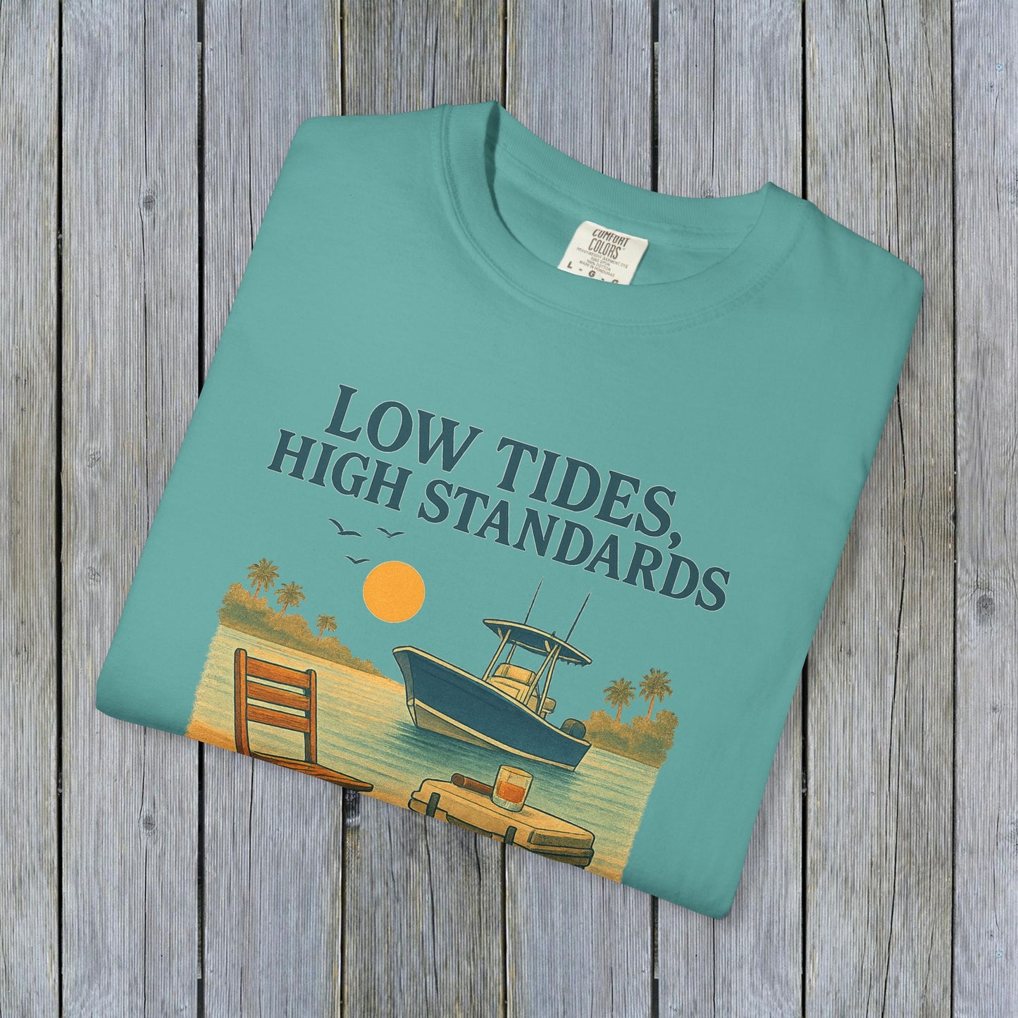 Folded Garment-Dyed Low Tides High Standards T-Shirt in teal, depicting a serene beach scene with a boat, ideal for comfortable casual wear.