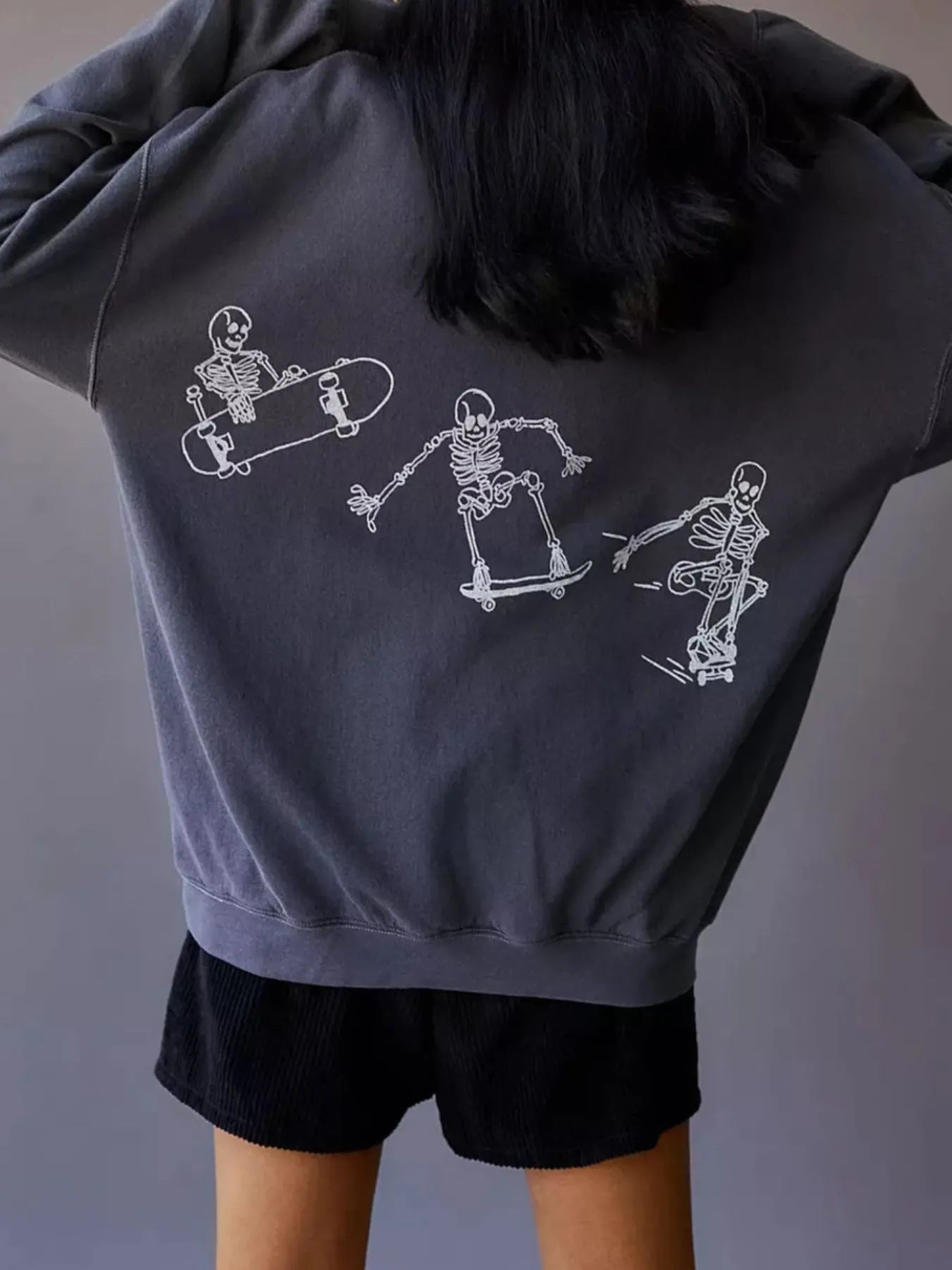 Back view of an Oversized Skeleton Graphic Sweatshirt for Women, displaying a dynamic skeleton skating design, constructed from slightly stretchy 100% polyester.