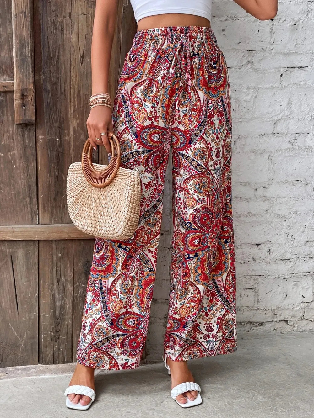 Model showcasing Trendy Printed Wide Leg Pants with Tied Detail in red paisley print, paired with a stylish handbag, crafted from 100% opaque polyester, perfect for fashion-forward looks.