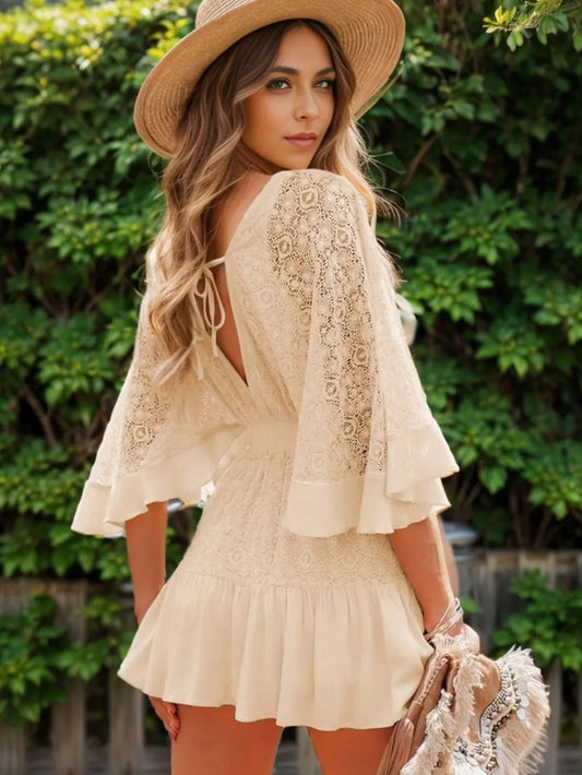 Woman wearing a semi-sheer ruffle hem lace mini dress with tie back, showcasing elegant smocked design, styled with a hat in an outdoor setting.