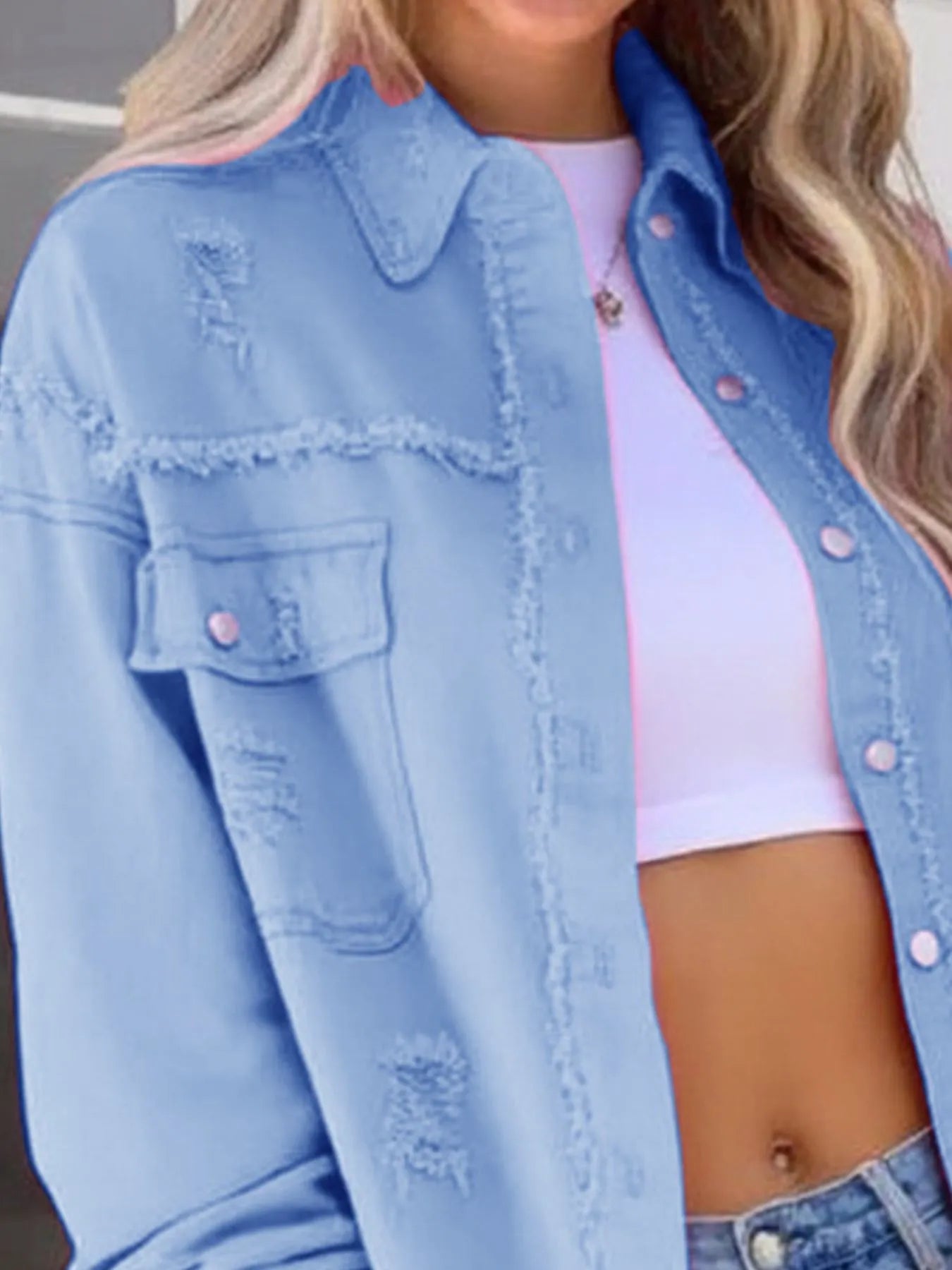 Close-up of Oversized Distressed Denim Jacket with Frayed Edges and Buttoned Pockets in pale blue, featuring fashionable details, worn over a white crop top, suitable for a casual look.