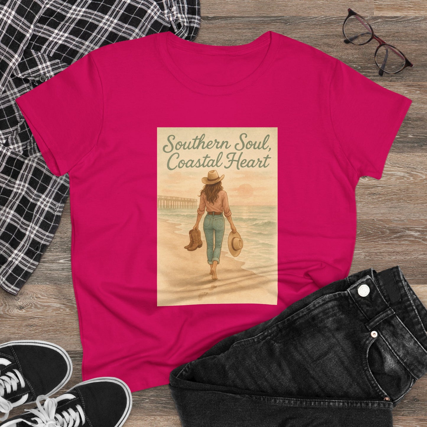 Southern Soul Coated Heart Tee displayed on a wooden surface, featuring a vibrant pink color and an artistic print of a woman walking towards the ocean, embodying a relaxed coastal vibe. Perfect for casual wear.