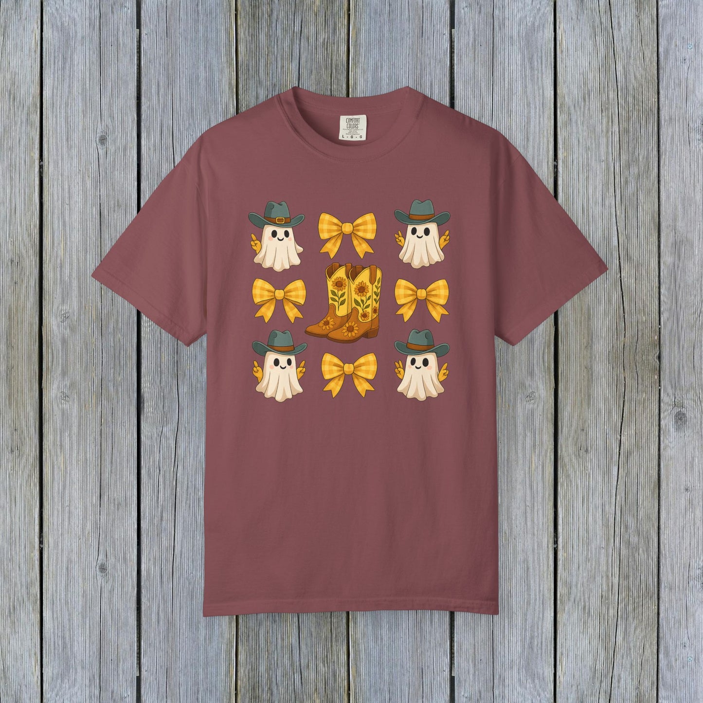 Cute Halloween T-Shirt on a rustic wooden background, featuring adorable ghosts, cowboy boots, and bows, showcasing fall fashion in eco-friendly material.