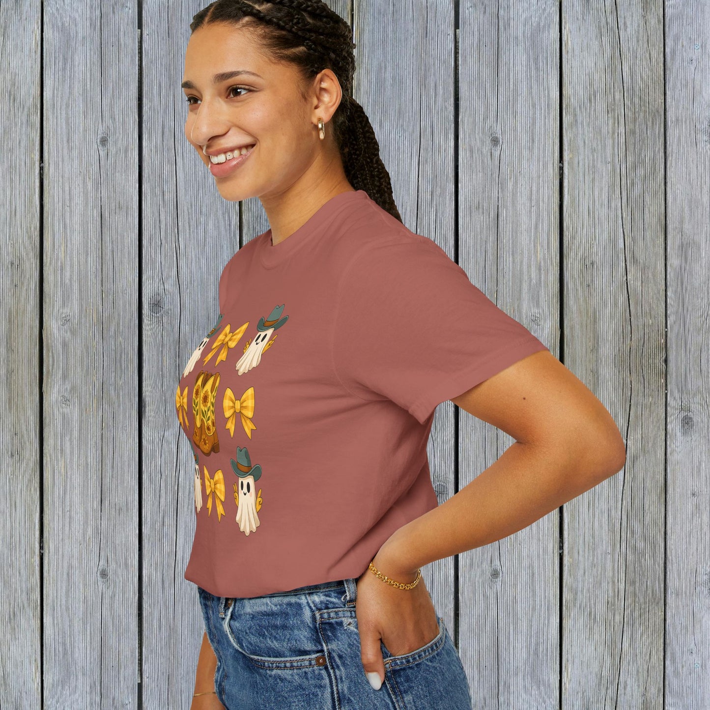 Cute Halloween T-Shirt worn by a woman with a cheerful smile in a side profile, featuring a fun design of ghosts and cowboy boots, perfect for unisex fall fashion and crafted from eco-friendly fabric.