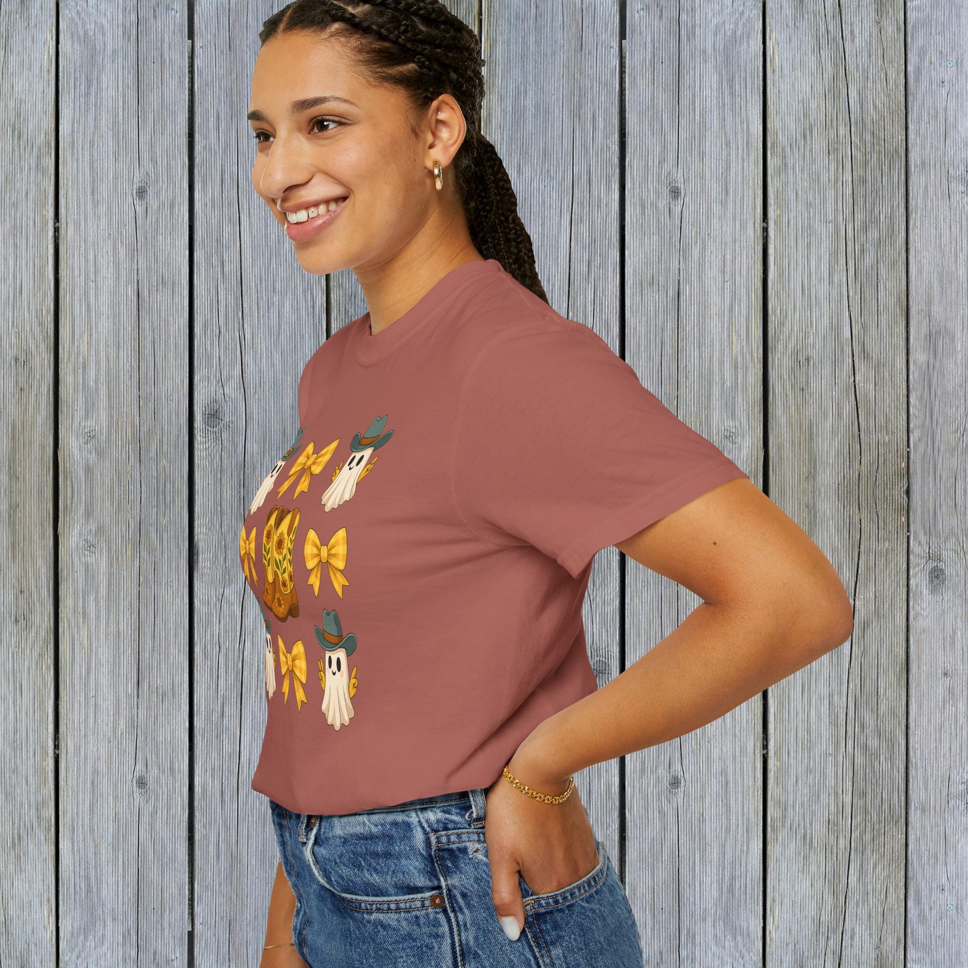 Cute Halloween T-Shirt worn by a woman with a cheerful smile in a side profile, featuring a fun design of ghosts and cowboy boots, perfect for unisex fall fashion and crafted from eco-friendly fabric.