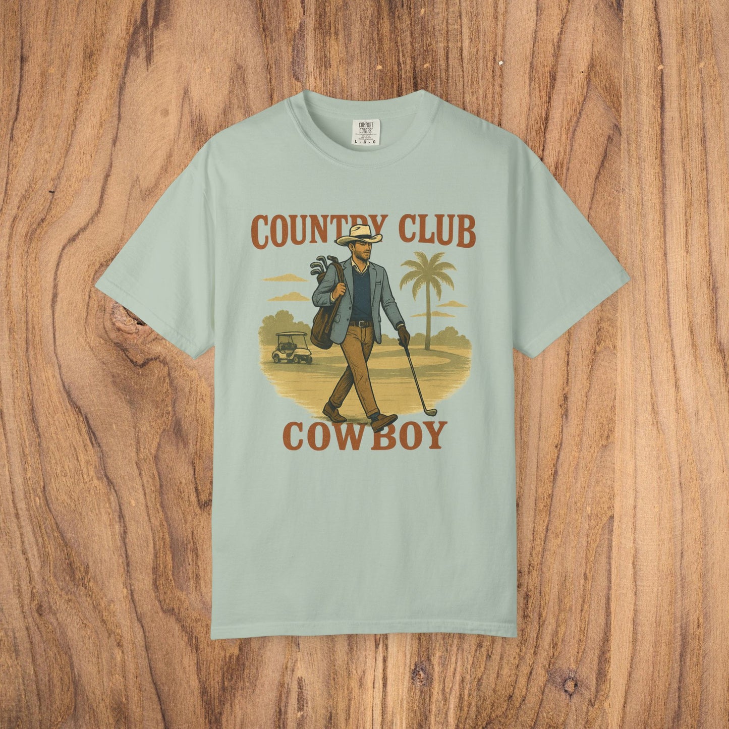 Country Club Cowboy Graphic Tee in light mint, illustrating a cowboy carrying golf equipment against a nature backdrop. Made from eco-friendly cotton, this shirt is both stylish and sustainable.