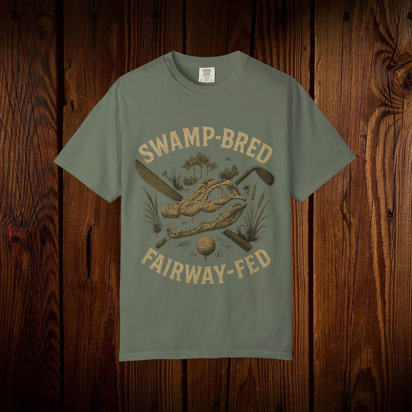 Unisex Swamp-Bred Fairway-Fed Tee in muted green, showcasing a unique alligator graphic with golf elements, ideal for golf enthusiasts.