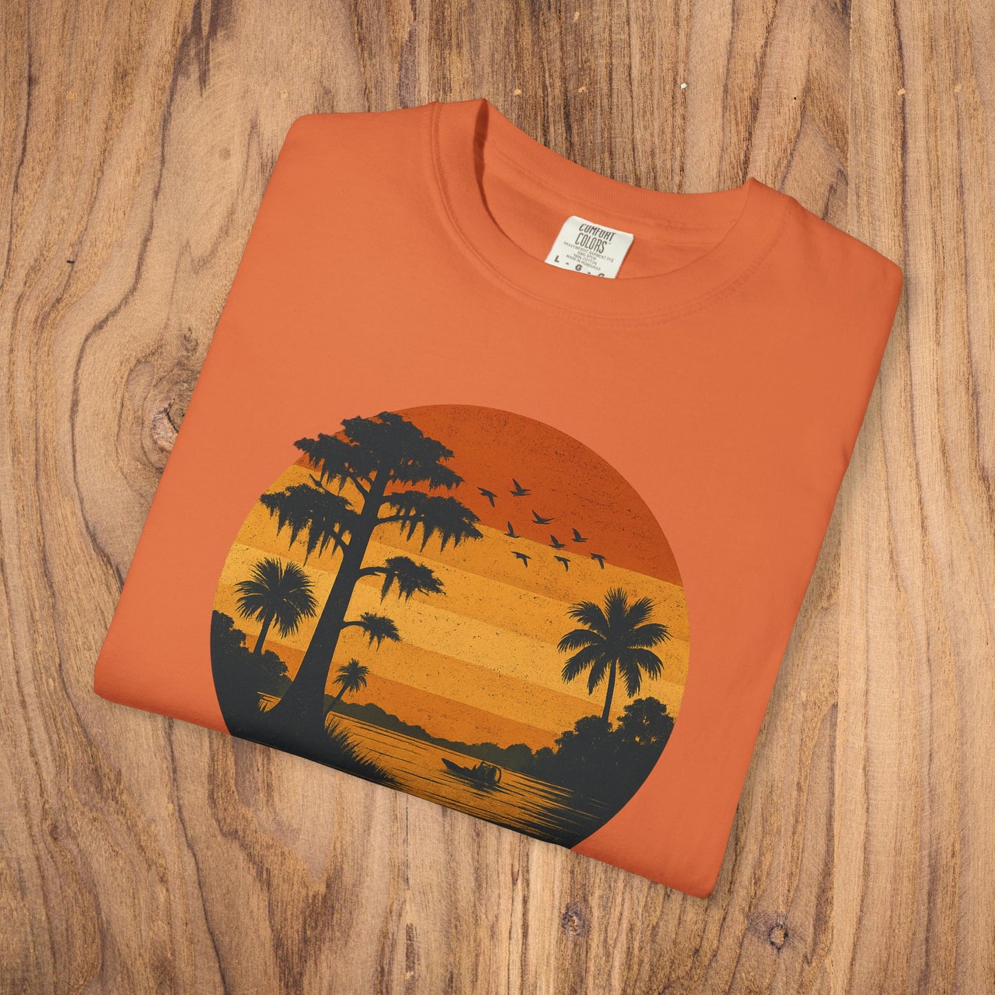 Unisex Garment-Dyed Sunset Tee in a bright orange hue, designed with a sunset and palm tree motif, made of soft 100% cotton for ultimate softness.