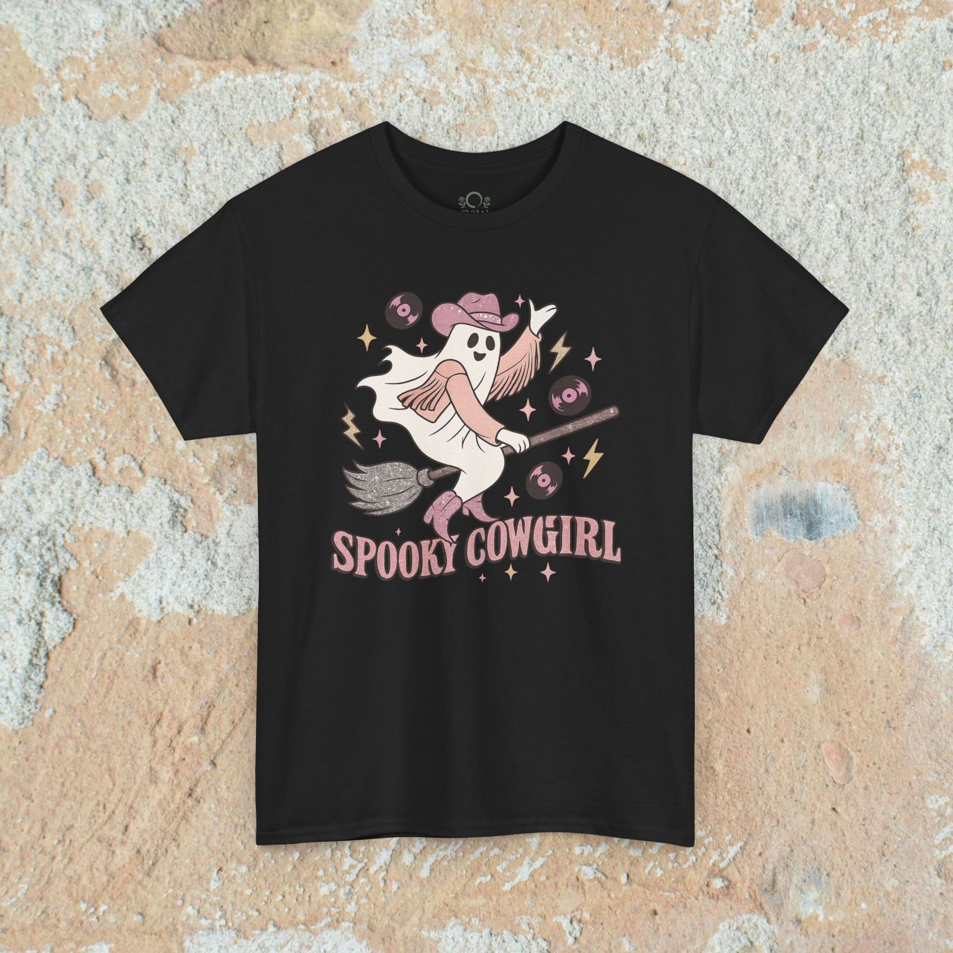 Spooky Cowgirl Graphic Tee featuring a playful ghost riding a broomstick with a cowboy hat, designed in vibrant colors on a black background.