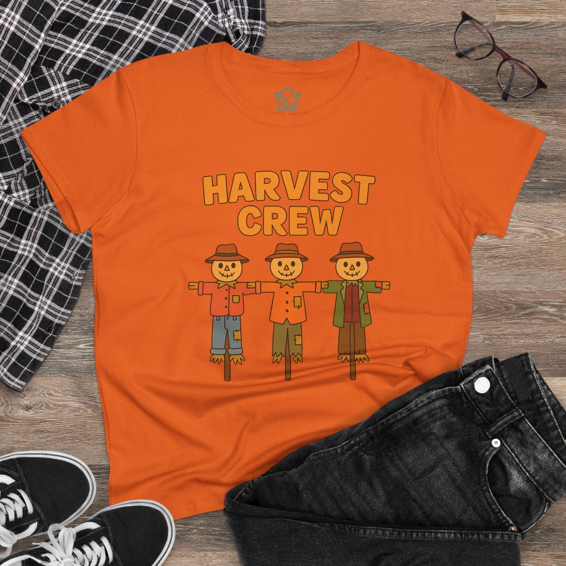 Harvest Crew Halloween T-Shirt featuring three cartoon scarecrows on an orange shirt, styled with casual black jeans and sneakers for a fun Halloween look.