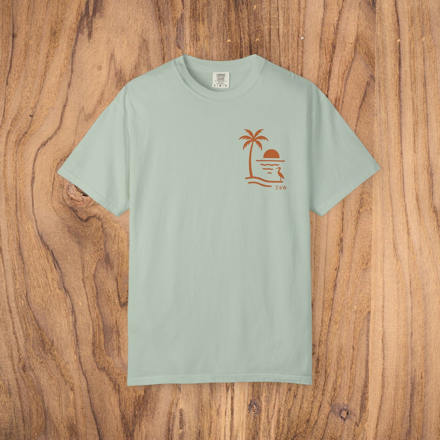Unisex Sunset Palm Tree T-Shirt in soothing mint green. This vibrant garment-dyed cotton tee is perfect for both men and women, featuring a palm tree and sunset design. Choose from 58 colors.