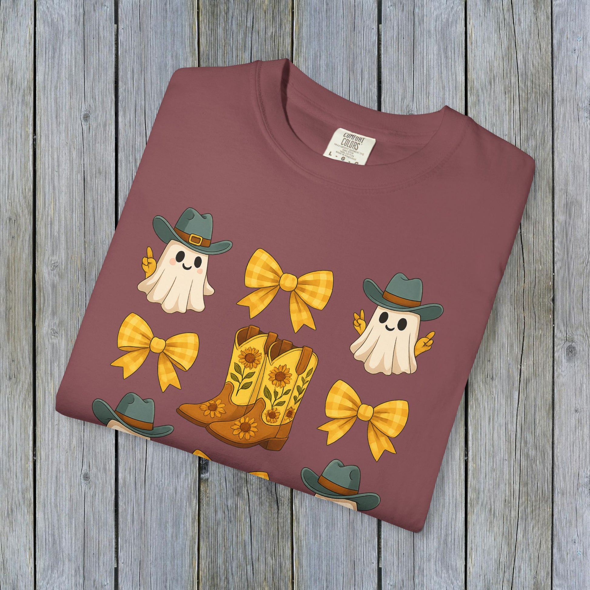Folded Cute Halloween T-Shirt showcasing ghosts, cowboy boots, and bows in a stylish maroon color. An ideal choice for eco-friendly unisex fall fashion.