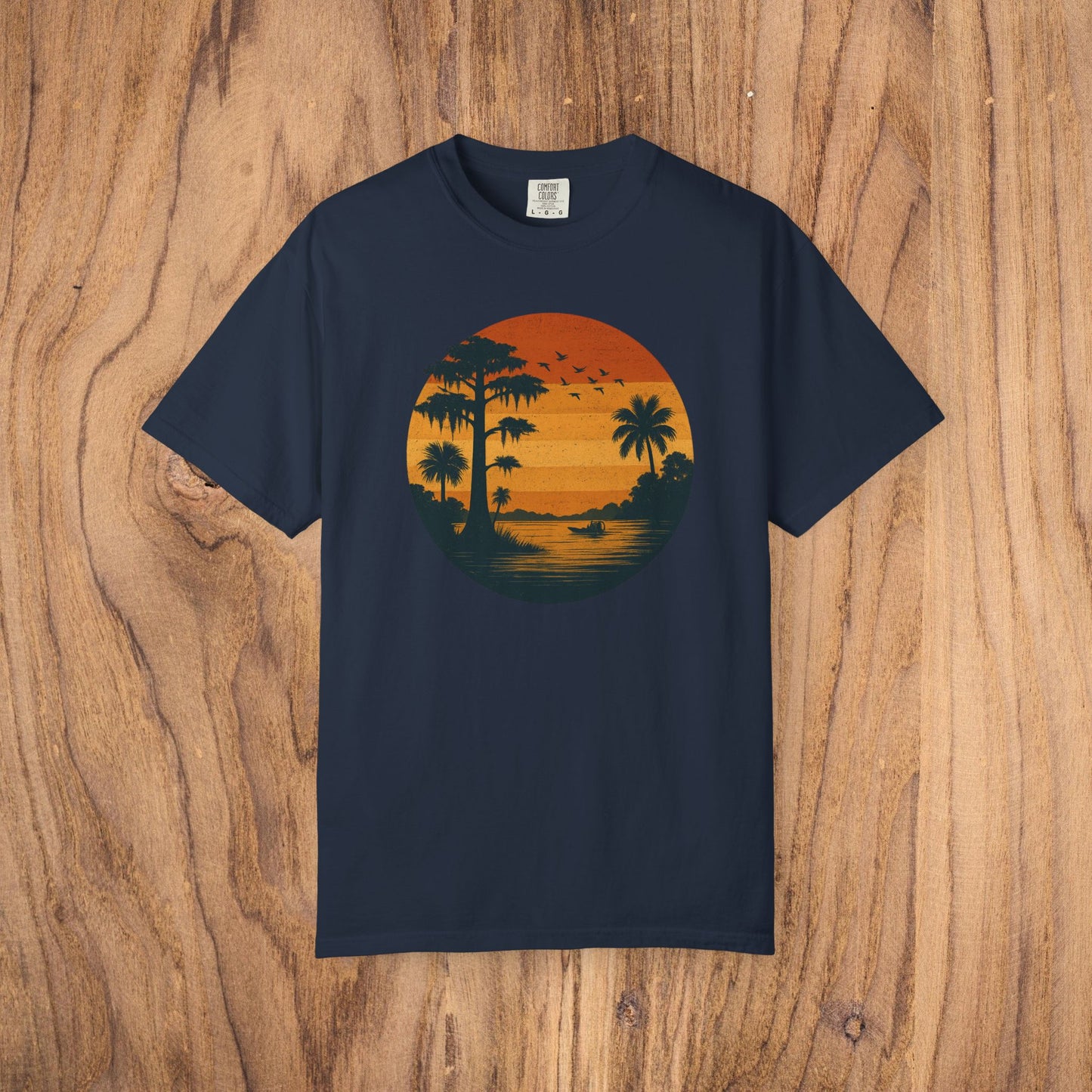Unisex Garment-Dyed Sunset Tee in classic navy blue displaying a gorgeous sunset graphic featuring silhouettes of palm trees and birds. Crafted from soft 100% cotton, available in sizes S to 4XL.