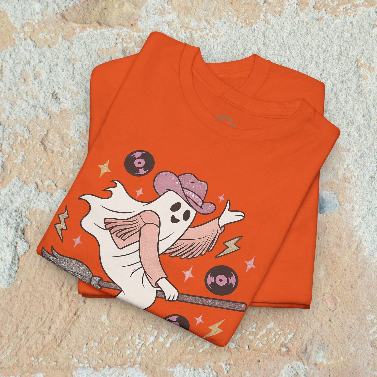 Stacked Spooky Cowgirl Graphic Tee with a fun design of a ghost in a cowboy hat, waving on a broomstick, highlighting its colorful, playful elements.