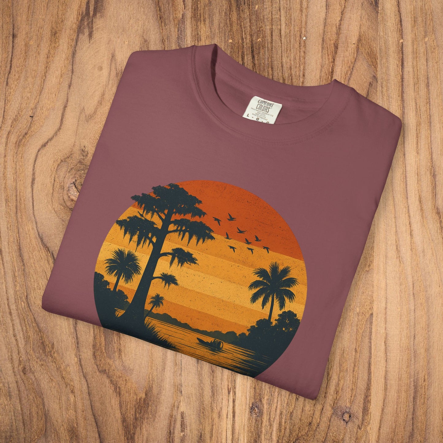 Unisex Garment-Dyed Sunset Tee in a rich maroon shade featuring an artistic sunset scene with palm trees, made from soft 100% cotton for comfort.