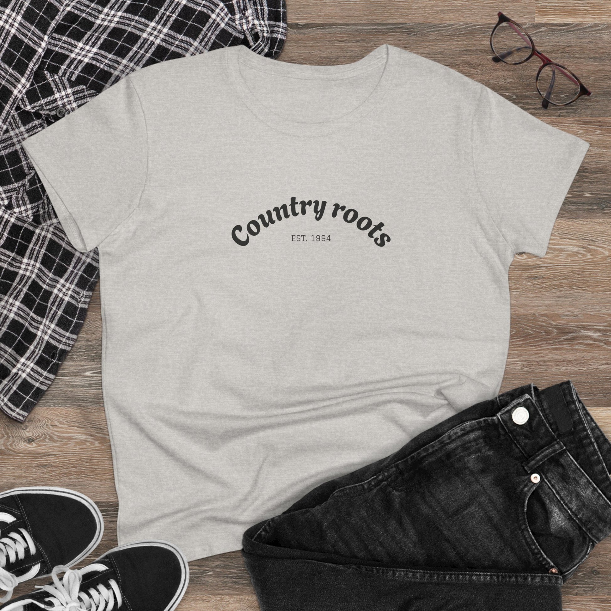 Country Roots Cowgirl Tee featuring a stylish 'Country roots EST. 1994' design, laid flat on rustic wooden background with casual outfit elements.