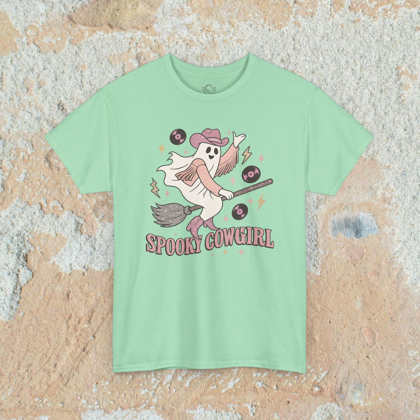 Spooky Cowgirl Graphic Tee in mint green, showcasing a cheerful ghost in a cowboy hat with a broomstick and vinyl records. Soft, sustainable fabric available in sizes S-5XL.