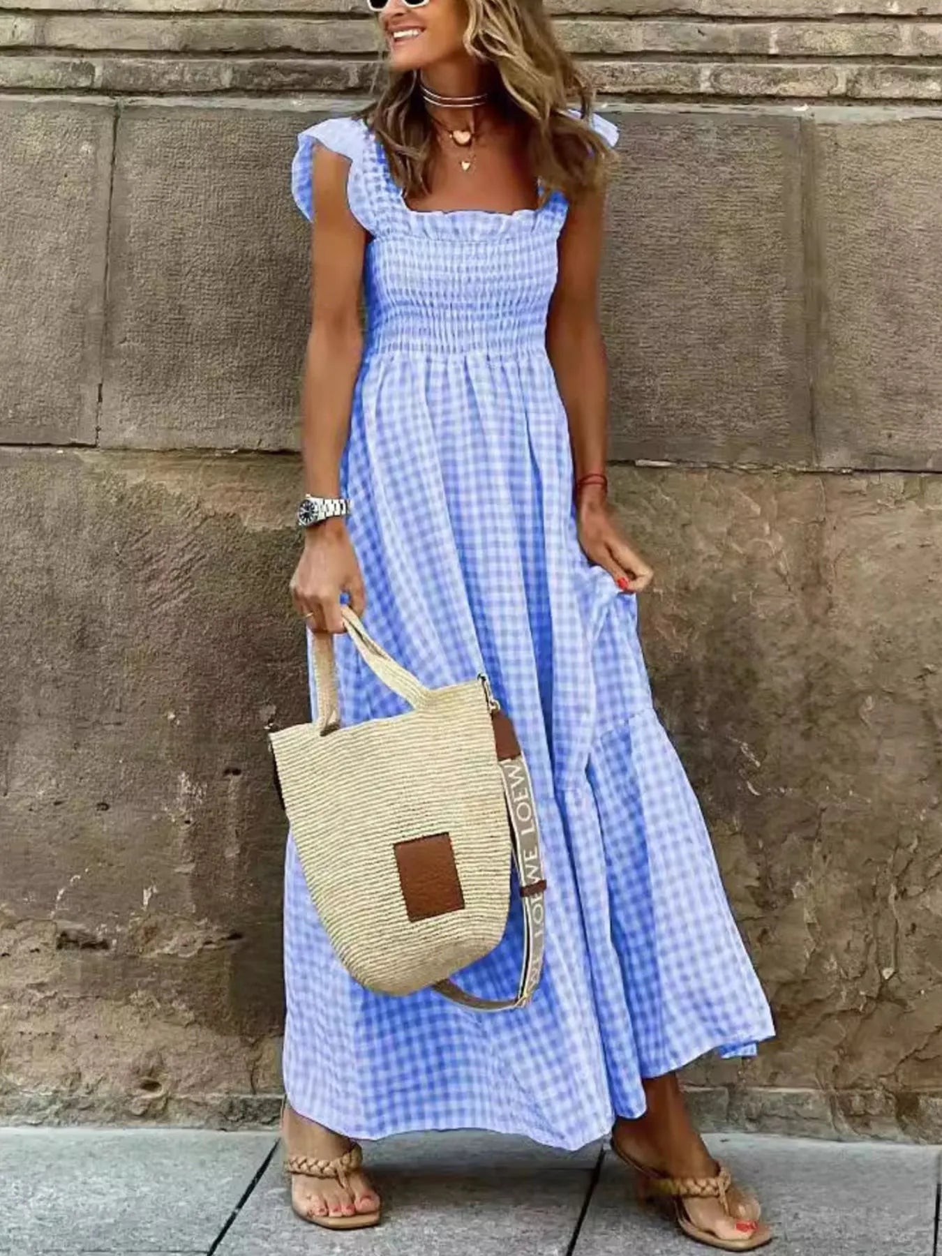 Fashionable lady in a blue Gingham Maxi Dress with Ruffle Straps, Smocked Bodice & Tiered Design by Trendsi, smiling and holding a stylish handbag in an urban setting.