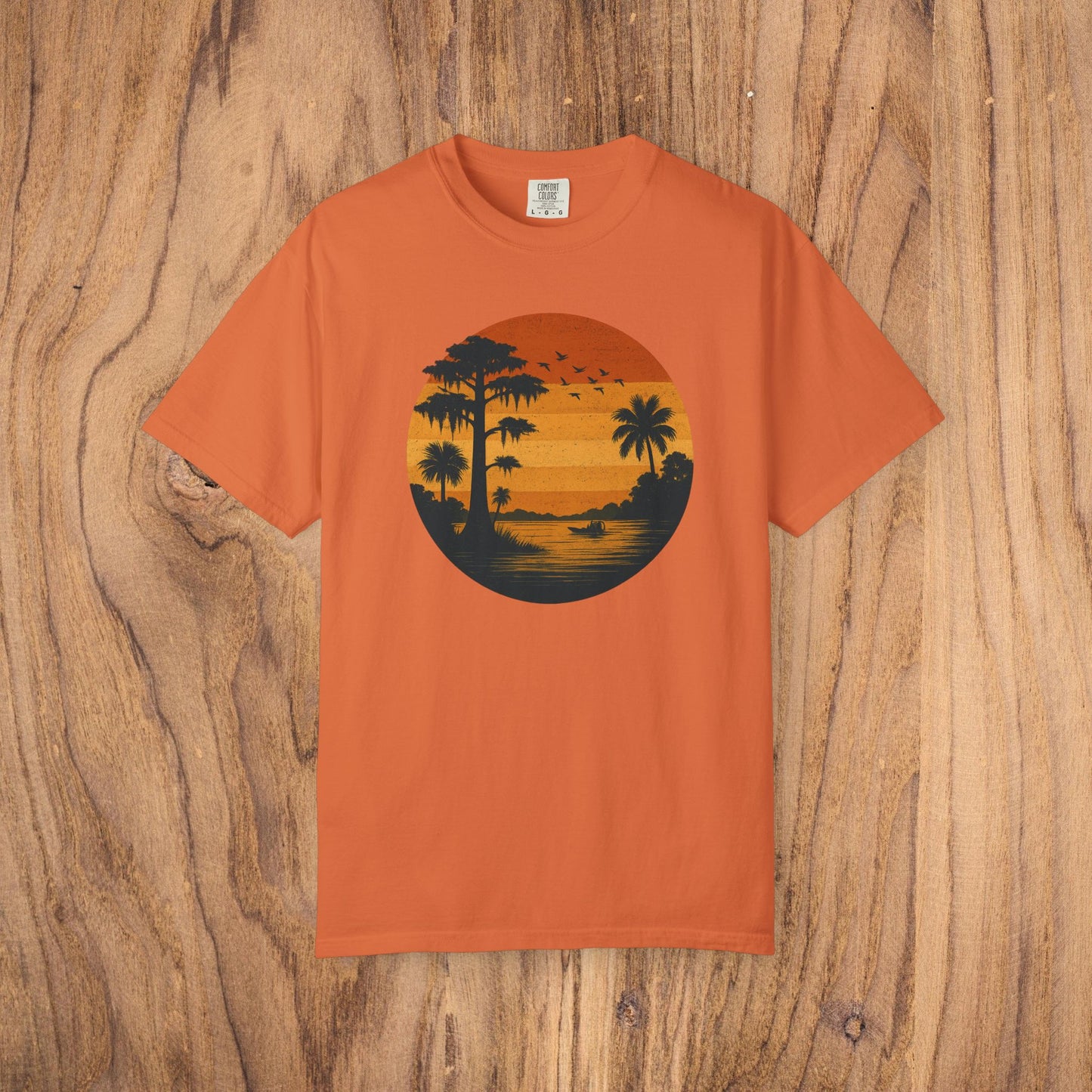 Unisex Garment-Dyed Sunset Tee in bright orange color showcasing a stunning sunset design with palm trees and flying birds. Made of soft 100% cotton, available in sizes S to 4XL.