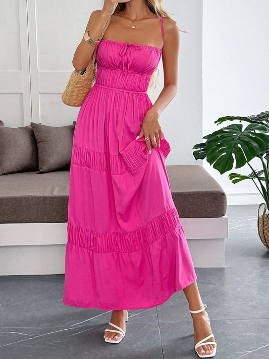 Side view of the Tied Back Tiered Maxi Cami Dress in bright pink, with a tiered skirt design, complemented by a wicker handbag and chic sandals.