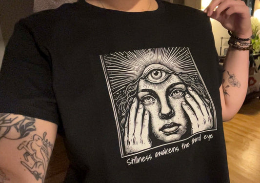 Stylish Third Eye Graphic Tee featuring a unique design with a woman holding her face, emphasizing the phrase 'Stillness awakens the third eye', made from 100% cotton, showcasing a cropped fit and durable comfort.