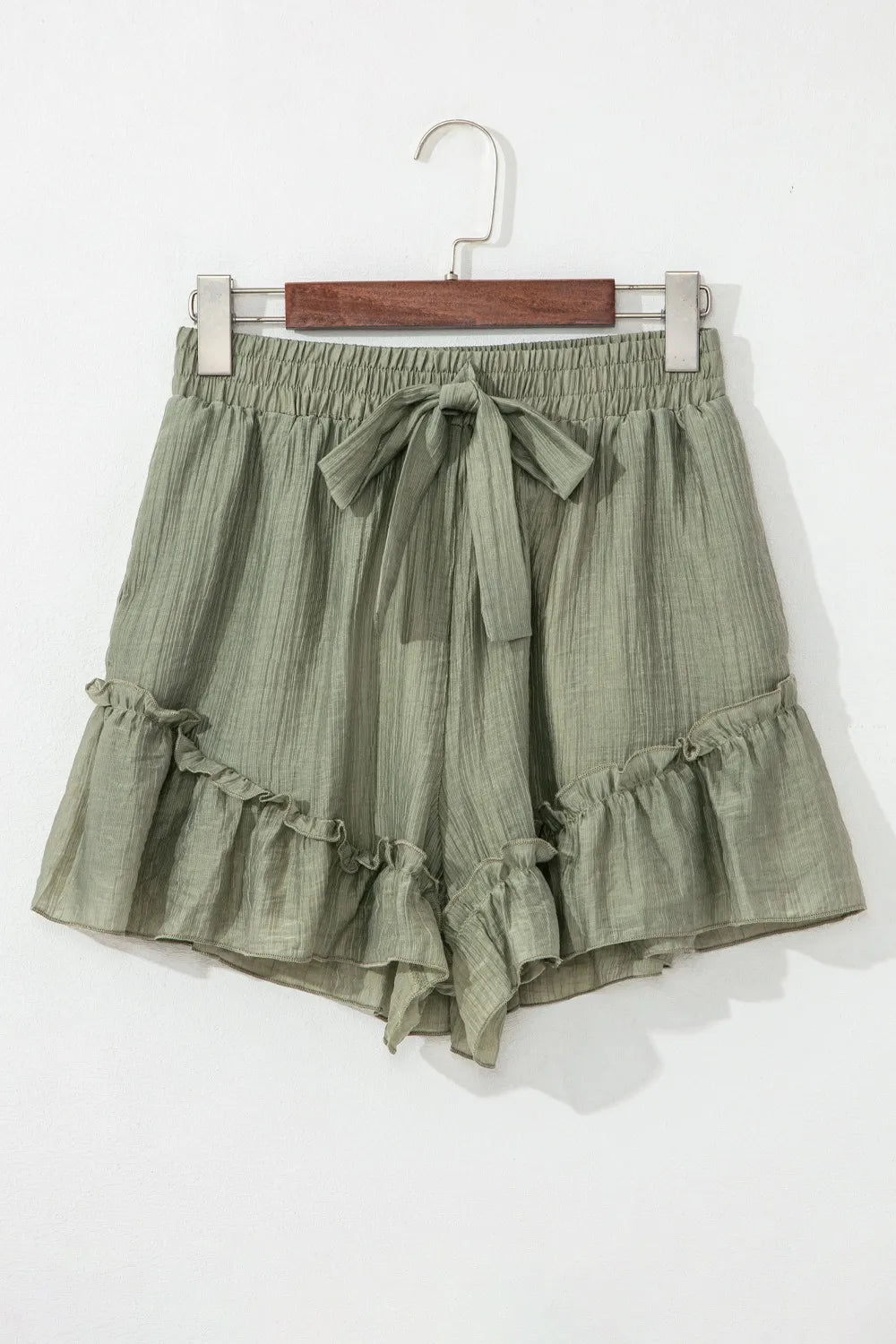 Textured Tie Waist Ruffle Hem Shorts in a soft olive green fabric, showcasing a stylish ruffle hem and a tie waist detail.
