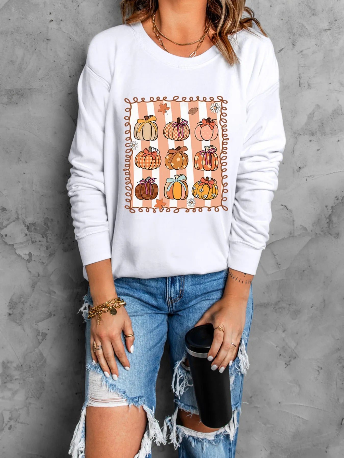 Model wearing the Slightly Stretchy Pumpkin Graphic Round Neck Sweatshirt for Fall, styled with distressed jeans and holding a black cup, embodying a casual, festive vibe.