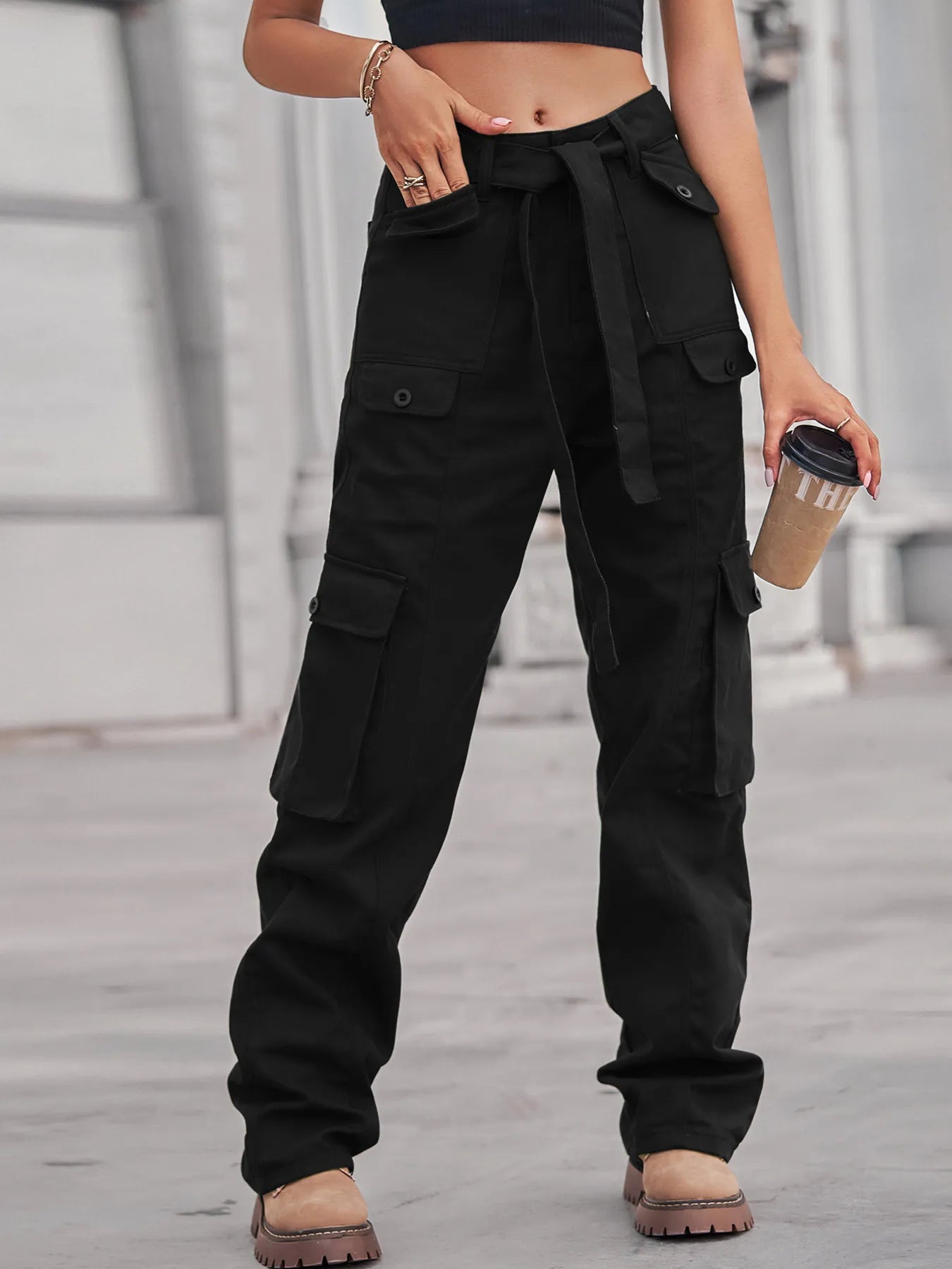 Fashionable model showcasing black High-Waisted Multi-Pocket Cargo Jeans, holding a coffee cup, styled with a cropped top for a modern vibe.