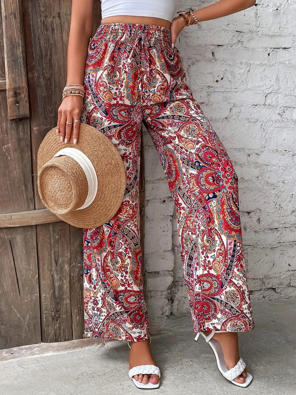 Model wearing Trendy Printed Wide Leg Pants with Tied Detail in vibrant red paisley pattern, accessorized with a straw hat, made from 100% opaque polyester, great for summer outings.