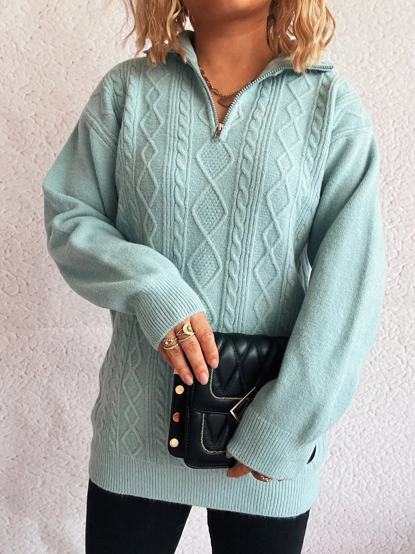 Model with a side pose wearing the Cozy Cable-Knit Texture Zip Collar Long Sleeve Sweater, accessorized with rings and holding a black handbag.