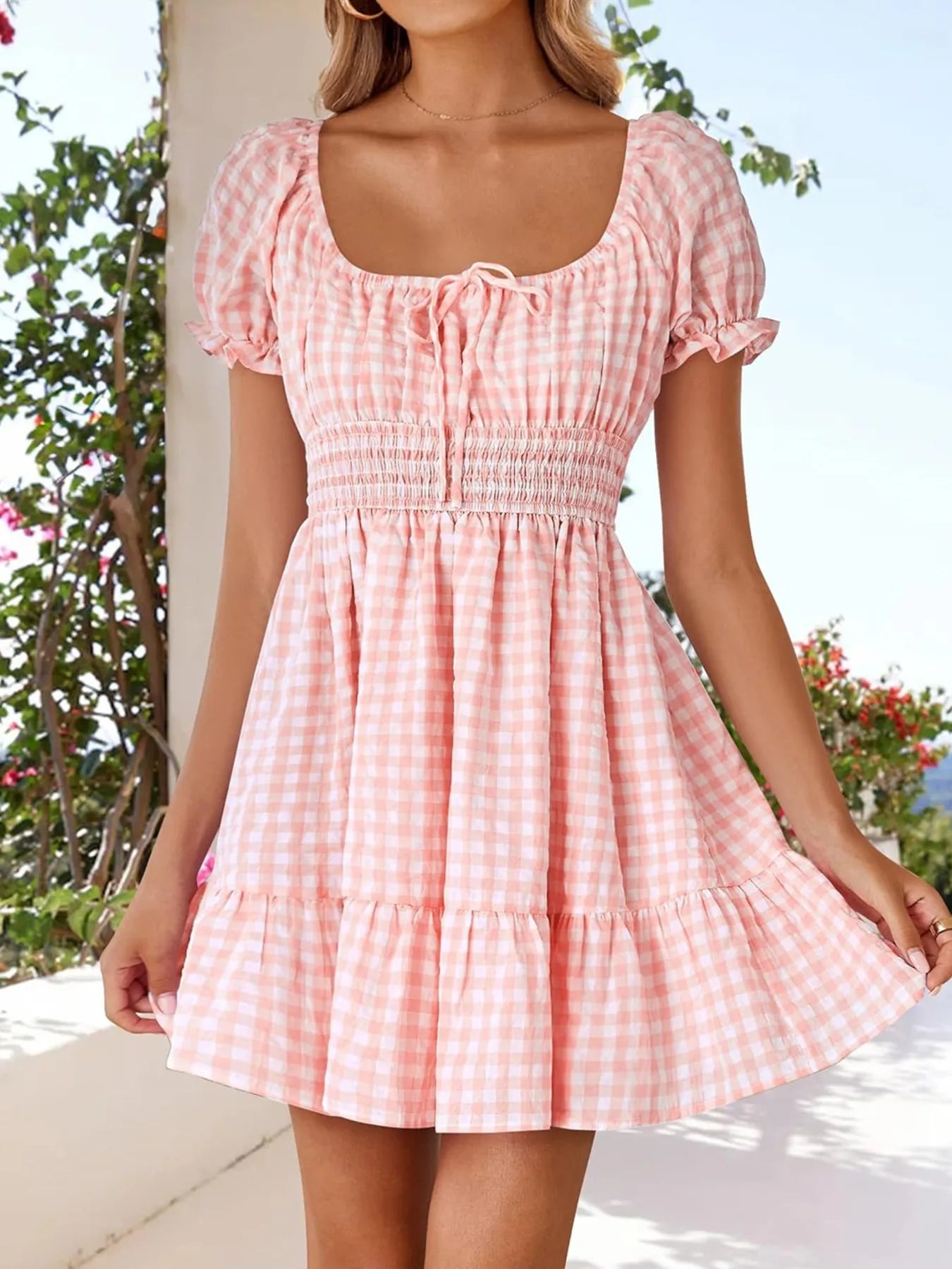 Model wearing Women's Gingham Puff Sleeve Smocked Dress in pink, demonstrating the flared skirt and puff sleeve design in a bright summer setting.
